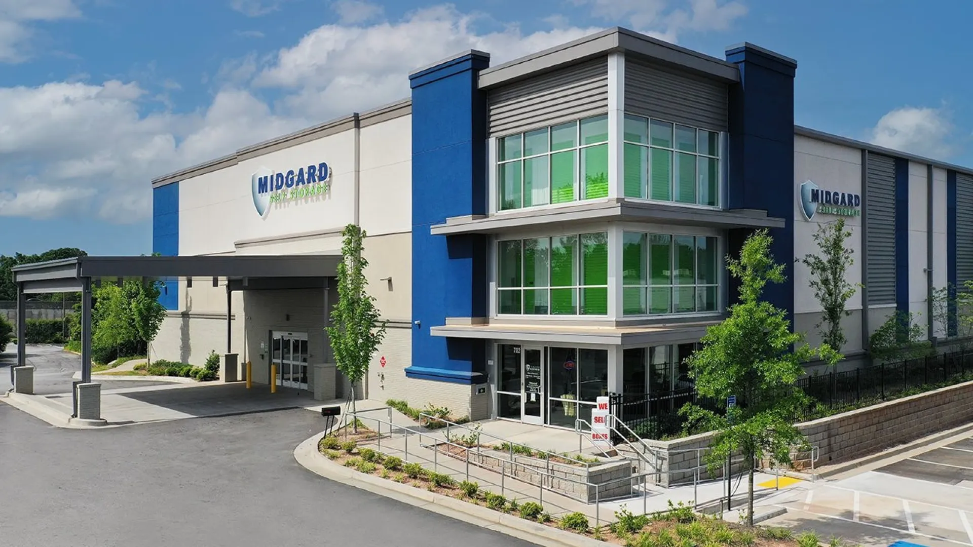 Modern Midgard building with blue accents, large windows, and landscaped surroundings under a partly cloudy sky.
