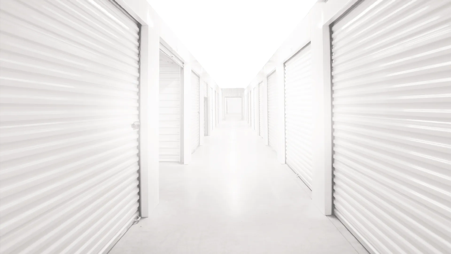 Bright white corridor with closed white metal storage unit doors on both sides in a storage facility.