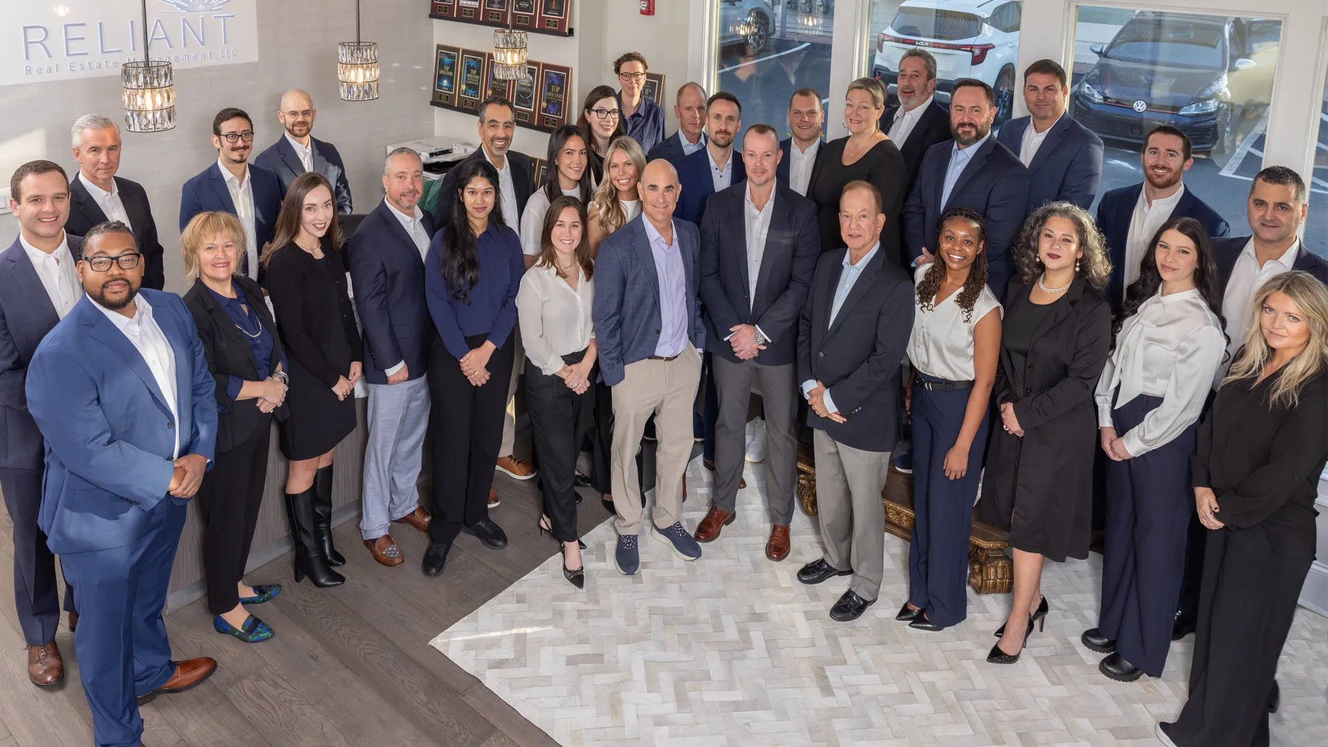 Large diverse group of professional men and women posing indoors in business attire for a team photo.