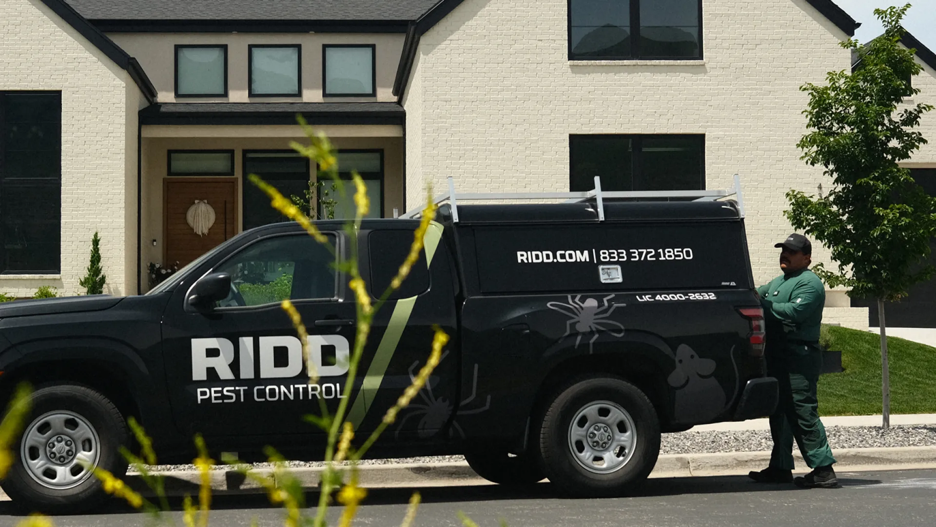 Ridd Pest Control black company vehicle parked in front of a modern white house with a technician nearby.