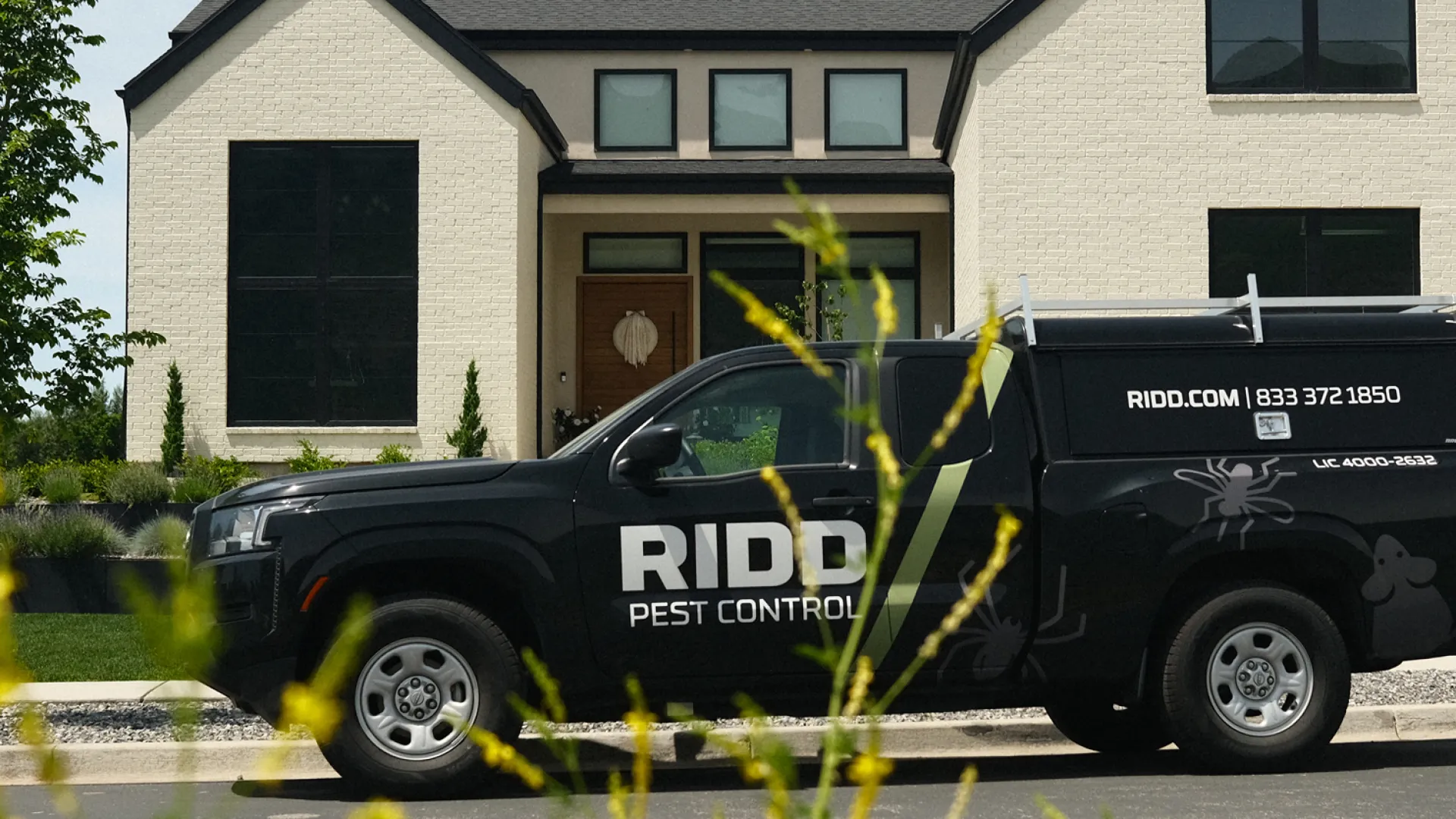 Black RIDDO Pest Control truck parked outside a modern suburban house with technician standing nearby.