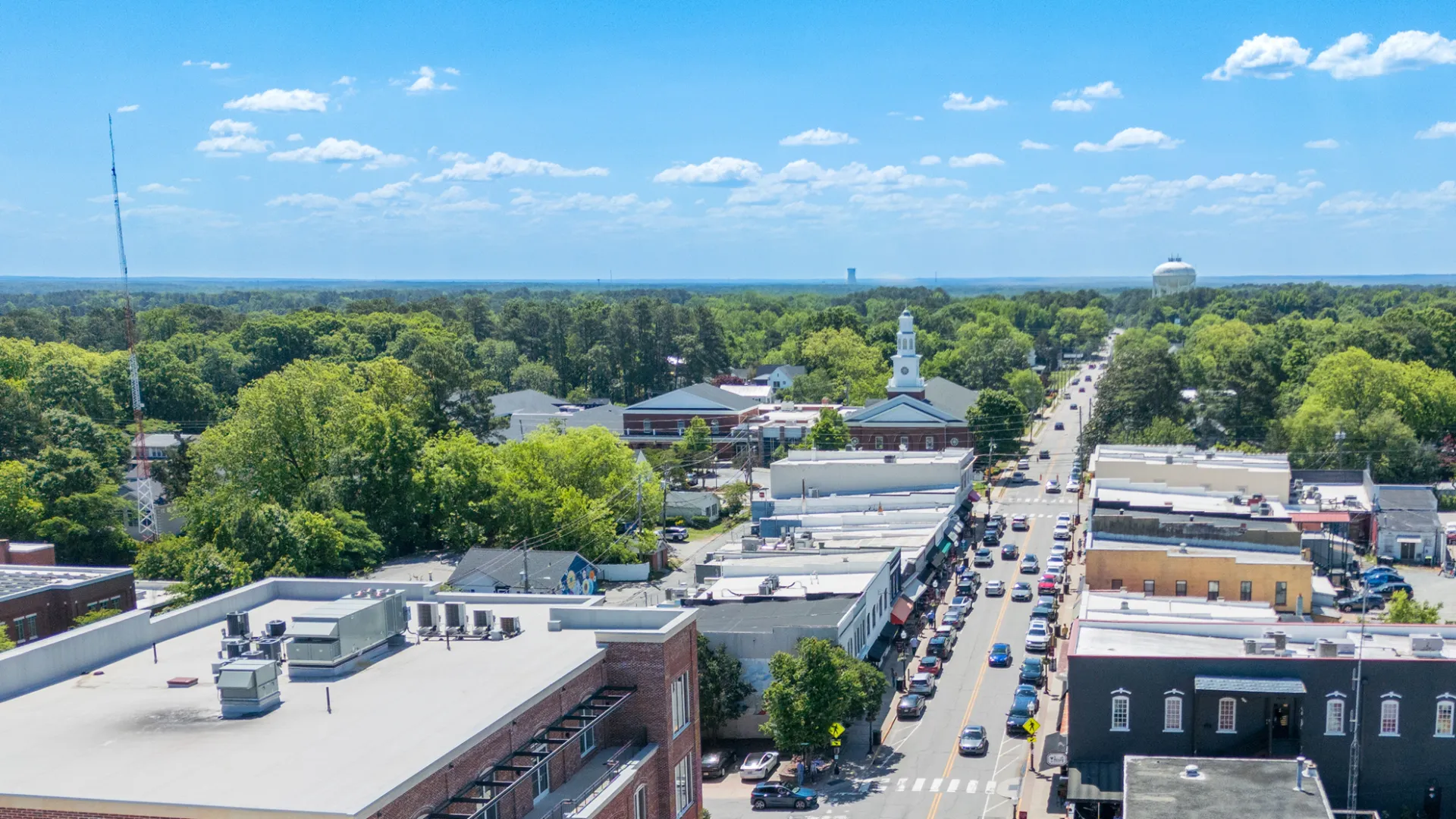 Aerial view of a small town with tree-lined streets, vehicles, and clear blue sky on a sunny day.
