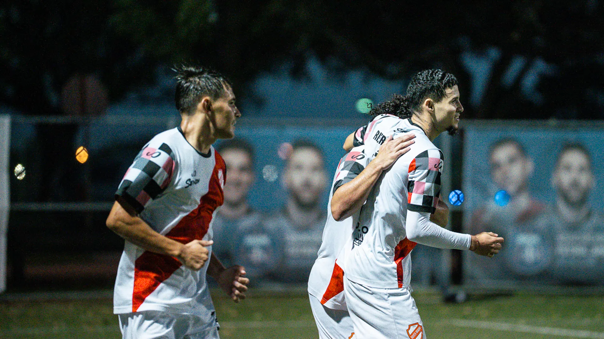 Soccer players in white and red uniforms celebrating on the field during a nighttime match.