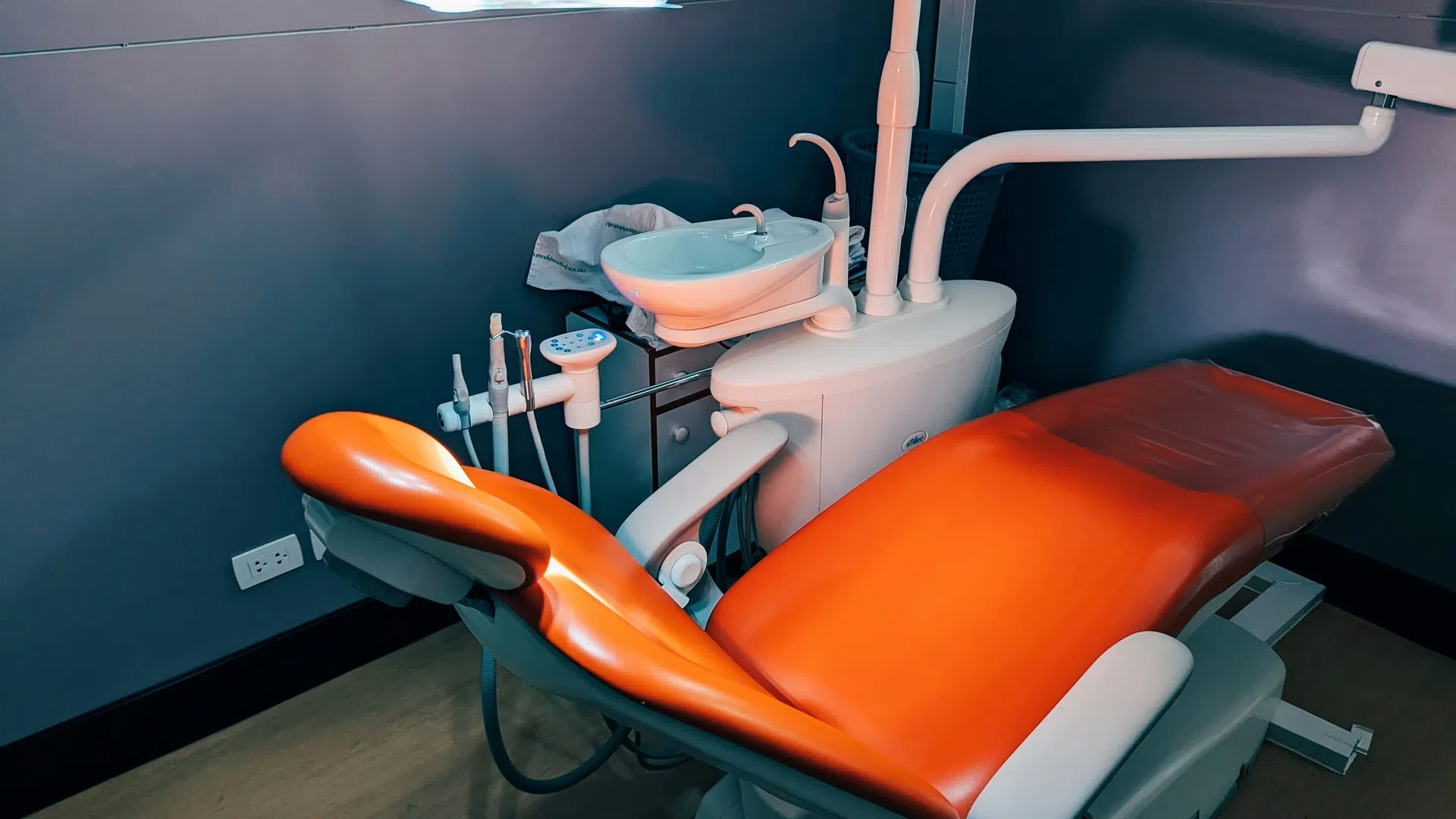 Modern dental chair with orange upholstery and dental tools in a softly lit clinic room.