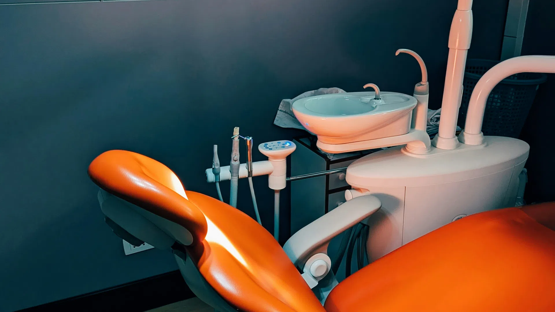 Orange dental chair and overhead light in a modern dental clinic treatment room setup.