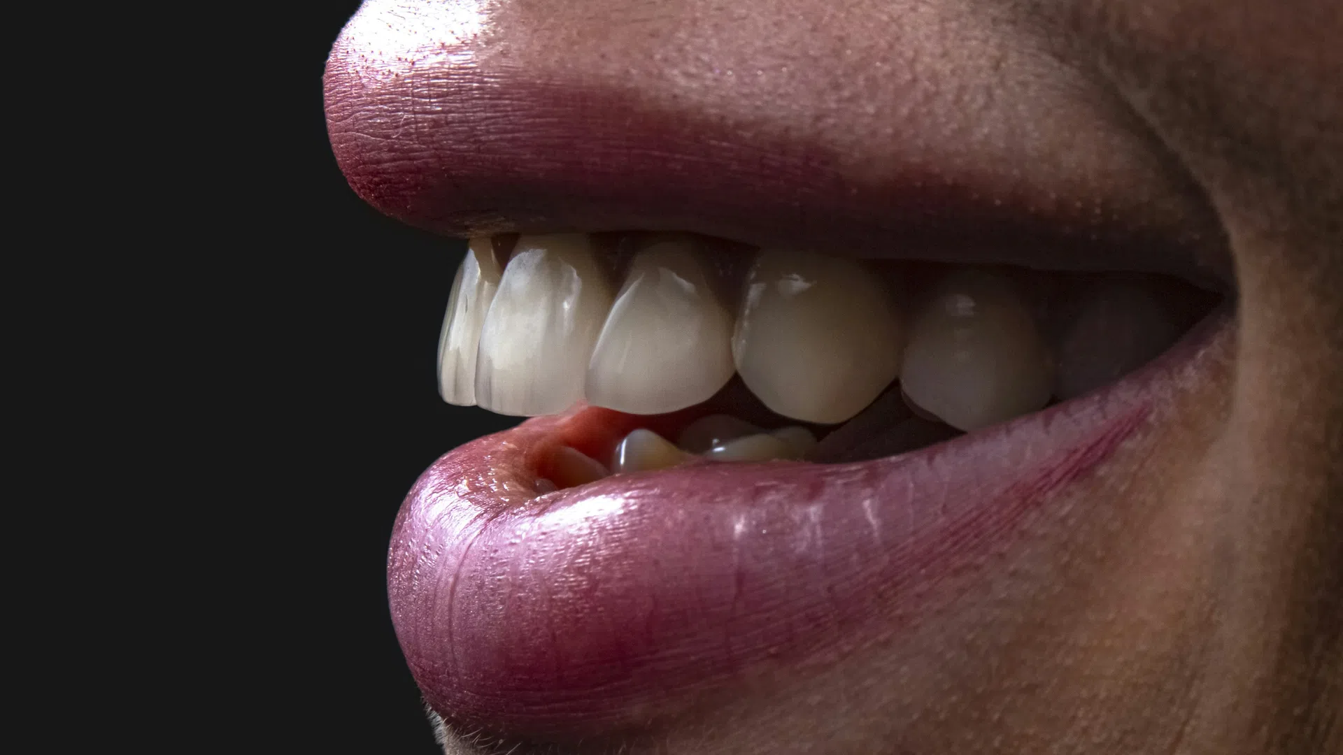 Close-up of a smiling mouth with lips and teeth against a black background.