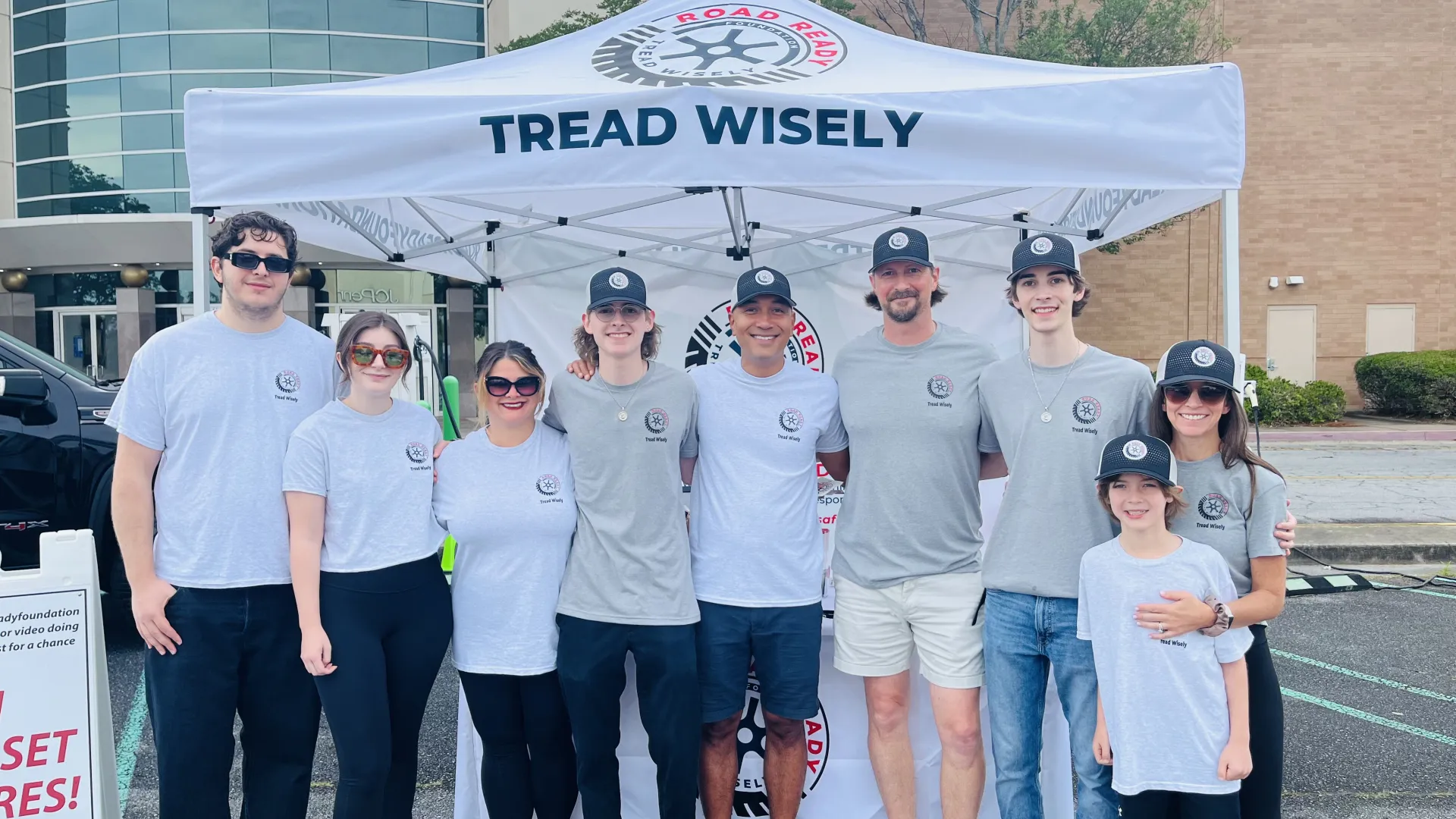 Group of nine people wearing matching t-shirts and caps standing in front of a tent with Tread Wisely logo.
