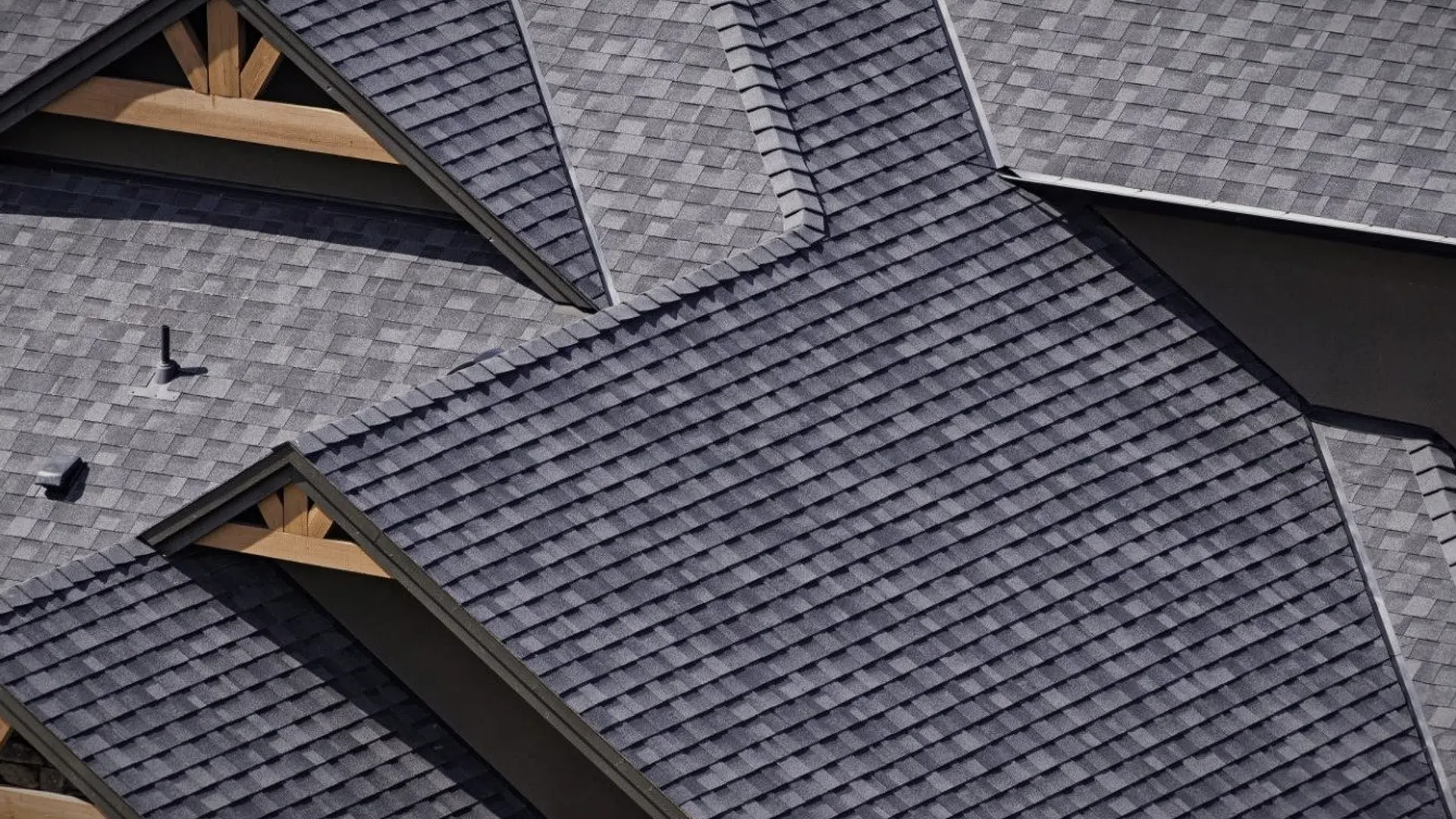 Close-up of dark gray asphalt shingle roofing with multiple gables and wooden trusses on a residential house.