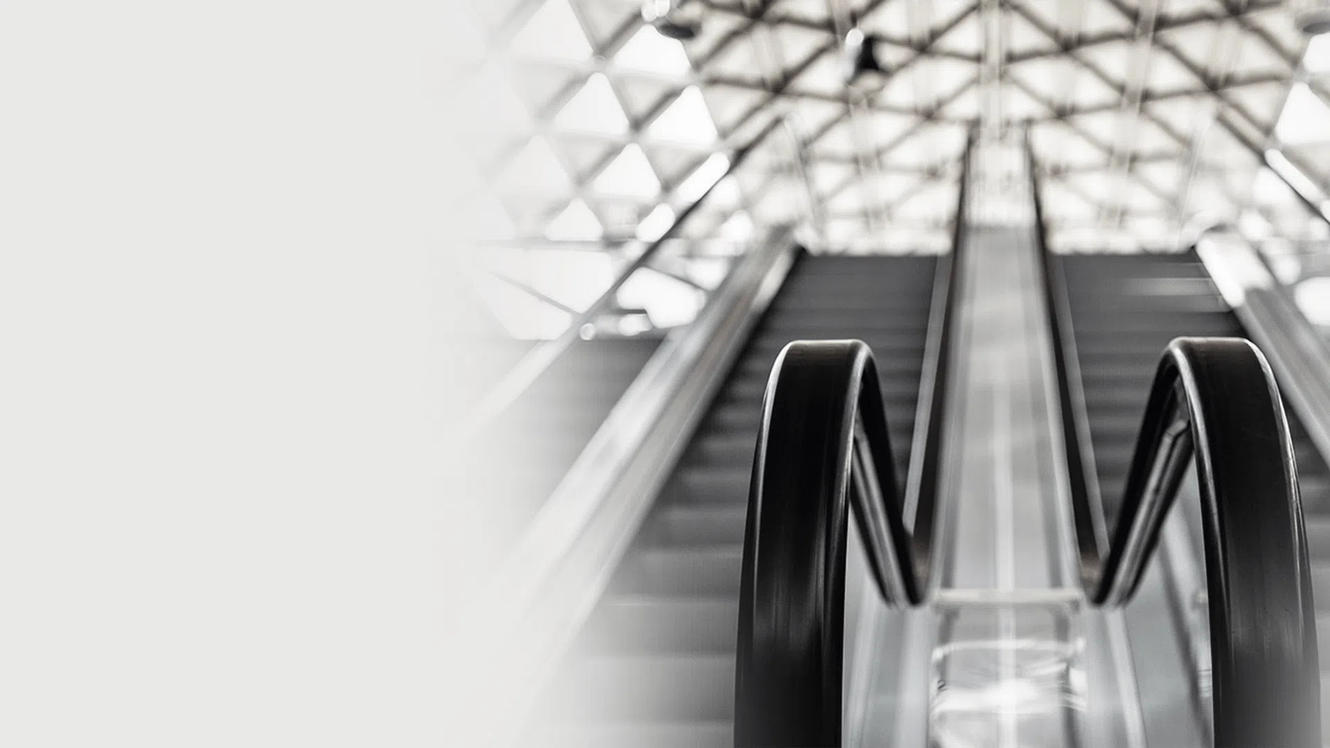 Black handrails and steps of a moving escalator with a bright geometric ceiling pattern above.