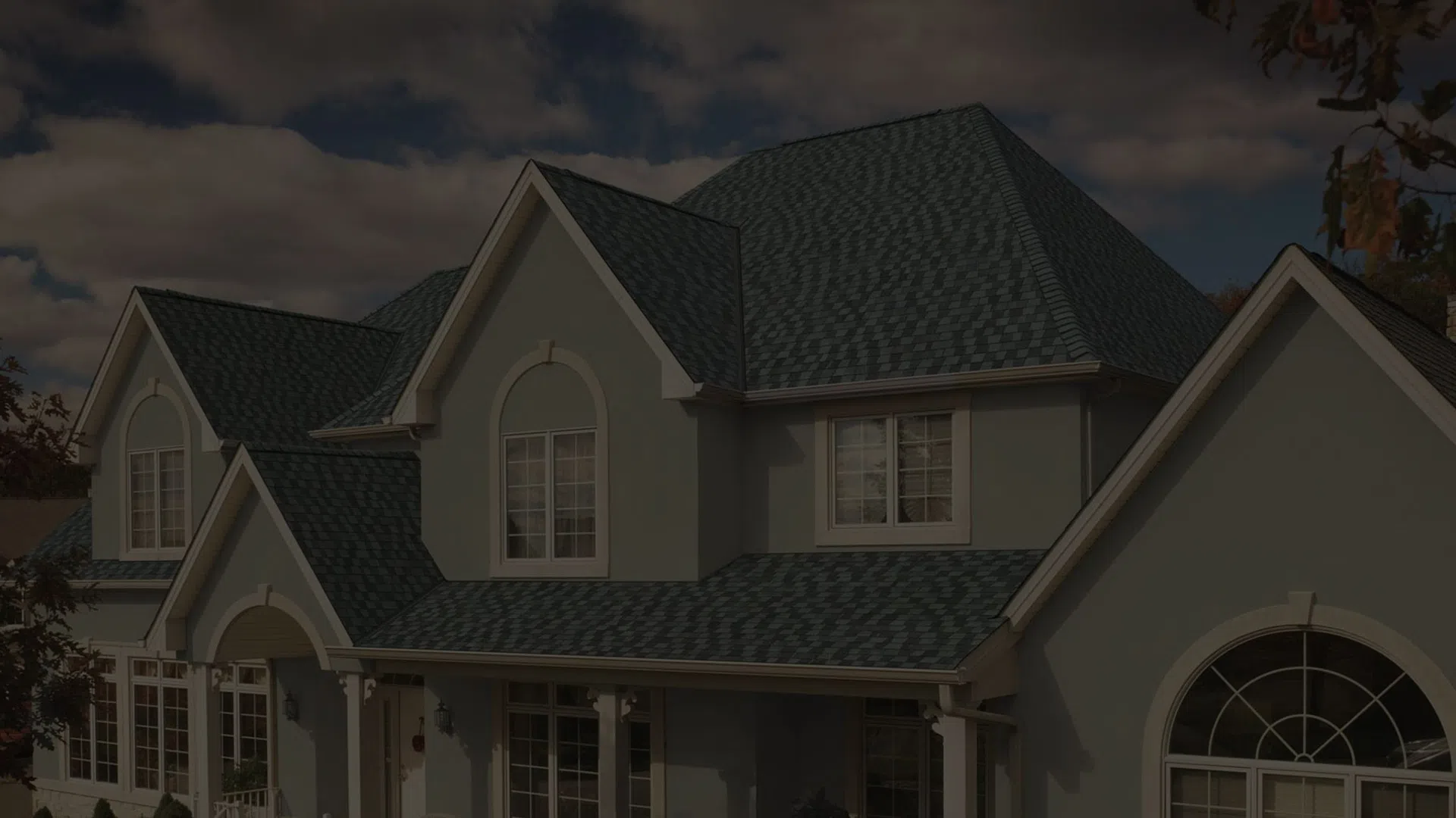 Large gray house with steep angled roof, white trim, multiple windows, and an arched window feature.