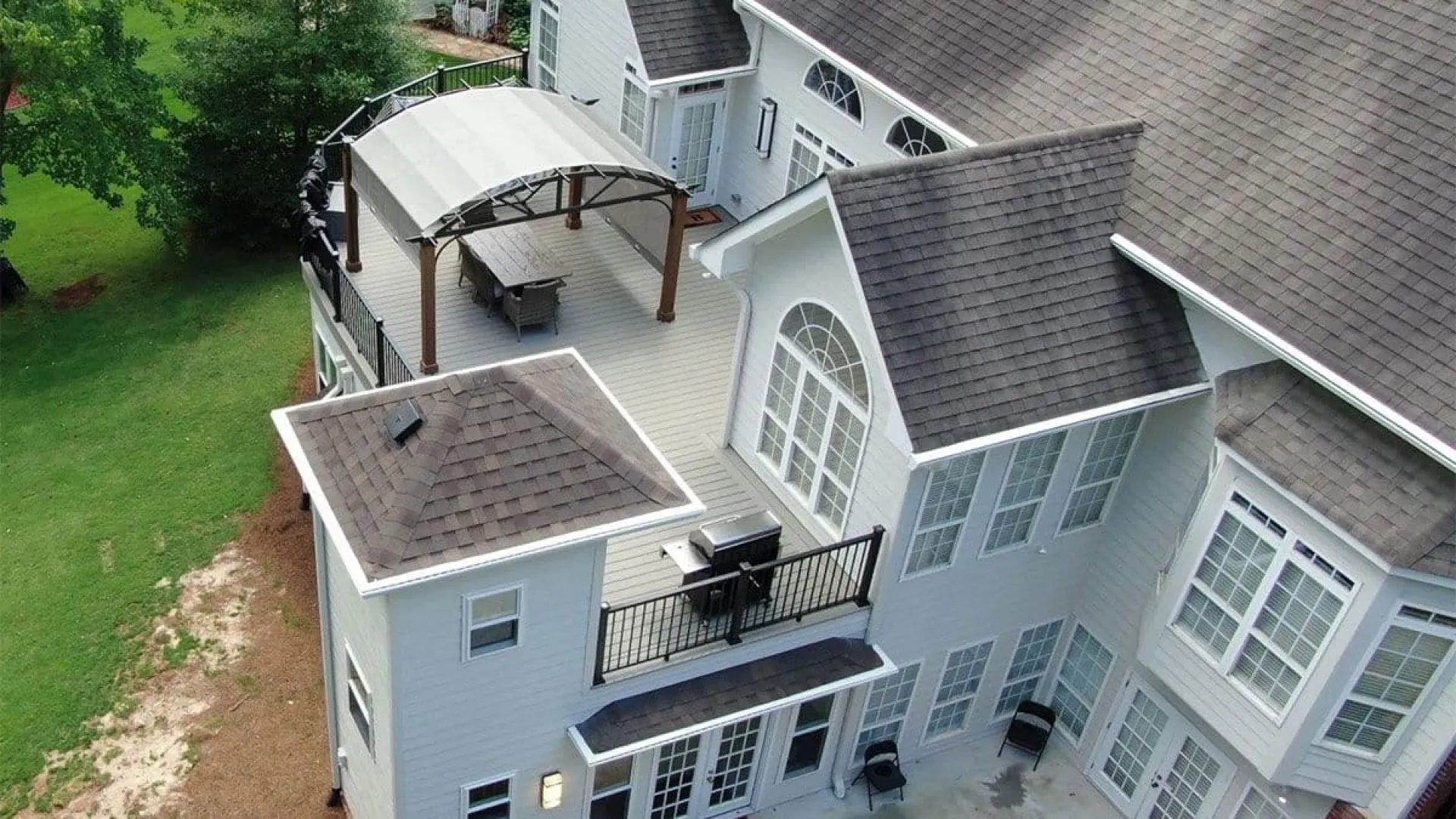 Aerial view of a large white house with multiple rooflines and a spacious deck featuring a covered seating area.