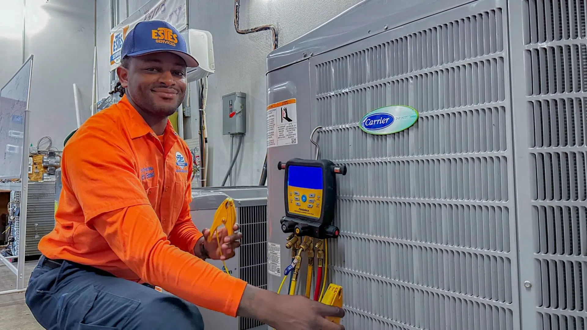 Technician in orange uniform working on Carrier HVAC unit using diagnostic tools indoors.