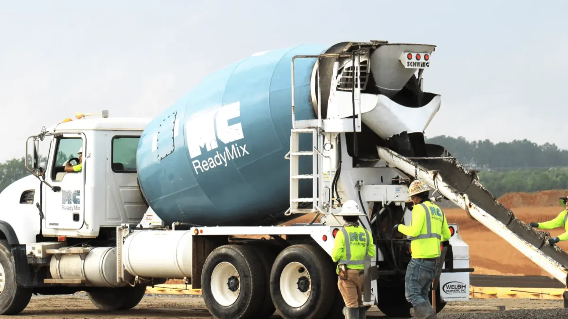 Concrete mixer truck pouring wet concrete at construction site with workers in safety gear monitoring process.