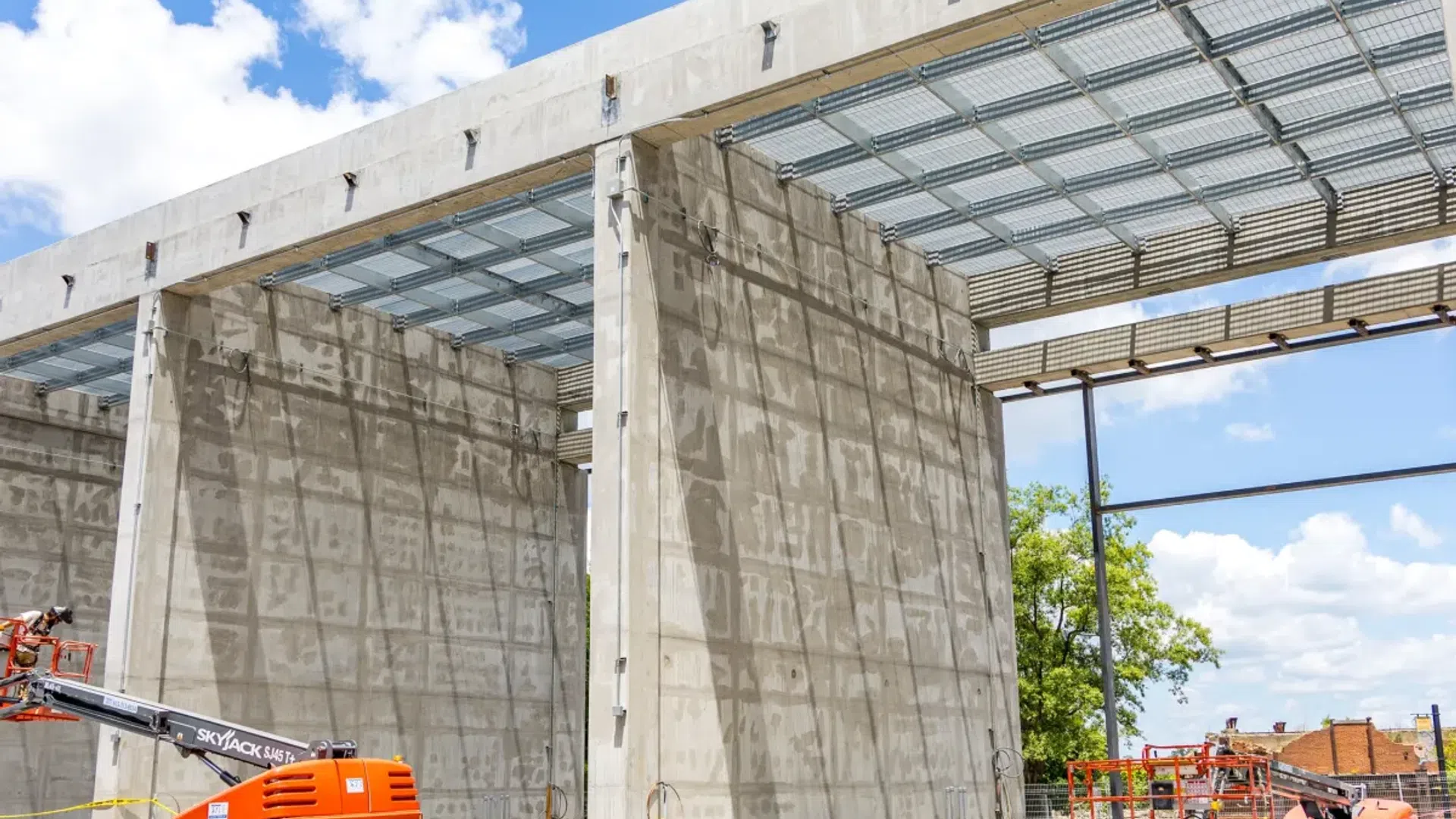 Construction site with large concrete structural walls, heavy machinery, steel beams, and blue sky background