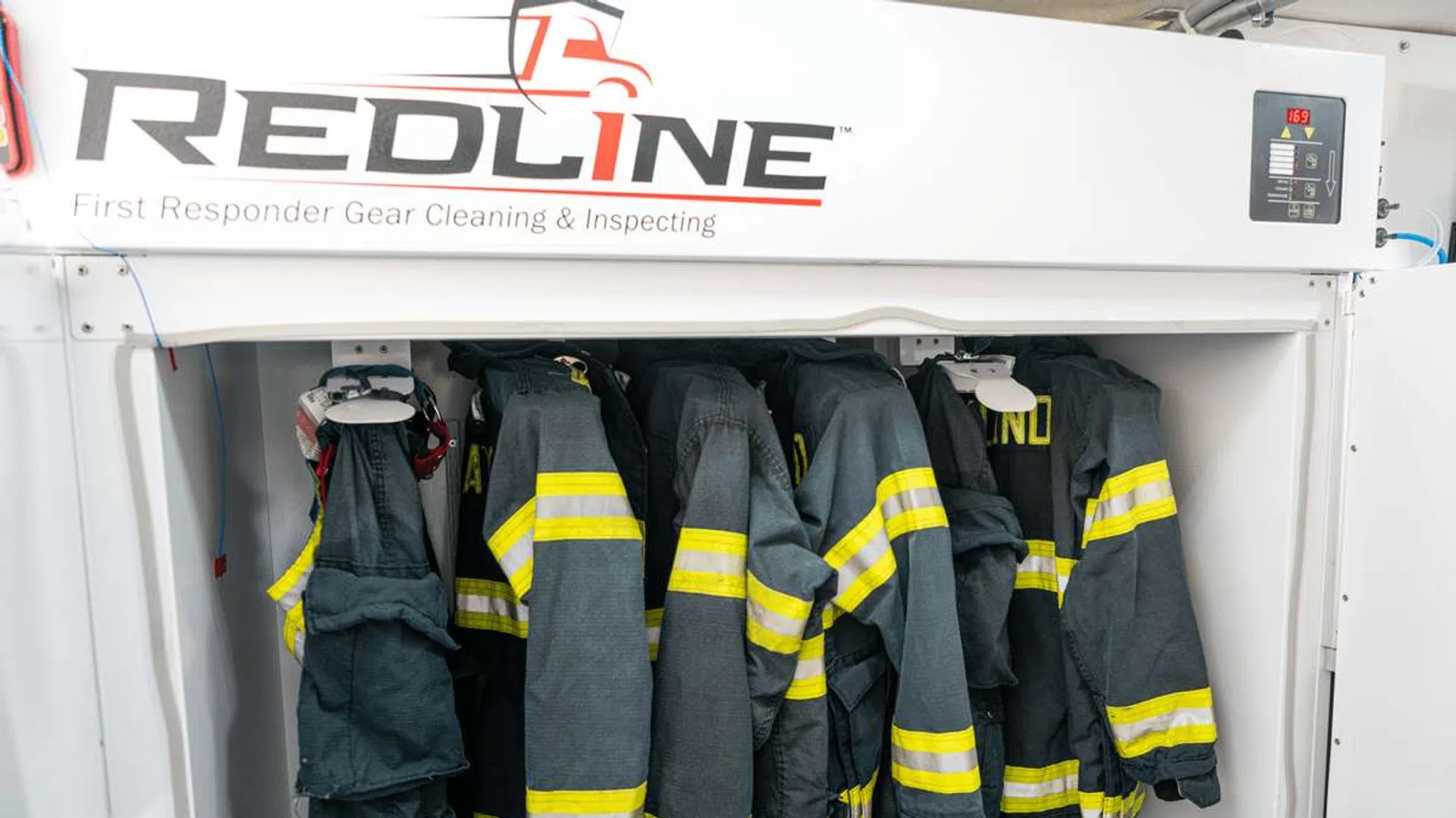 Firefighter turnout gear hanging inside REDLINE cleaning and inspection machine with yellow reflective stripes