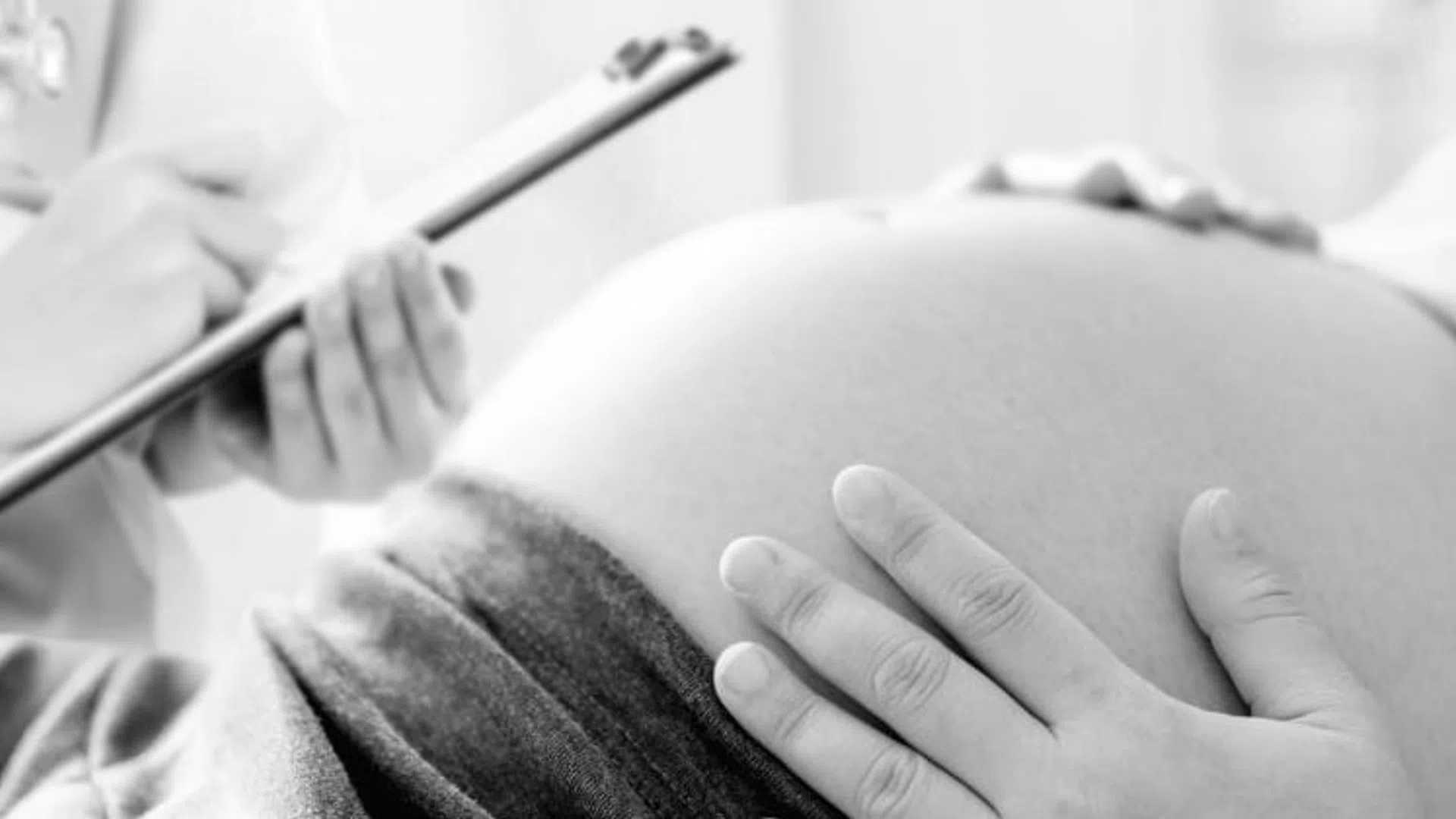 Pregnant woman with doctor holding clipboard and stethoscope during prenatal checkup in medical clinic