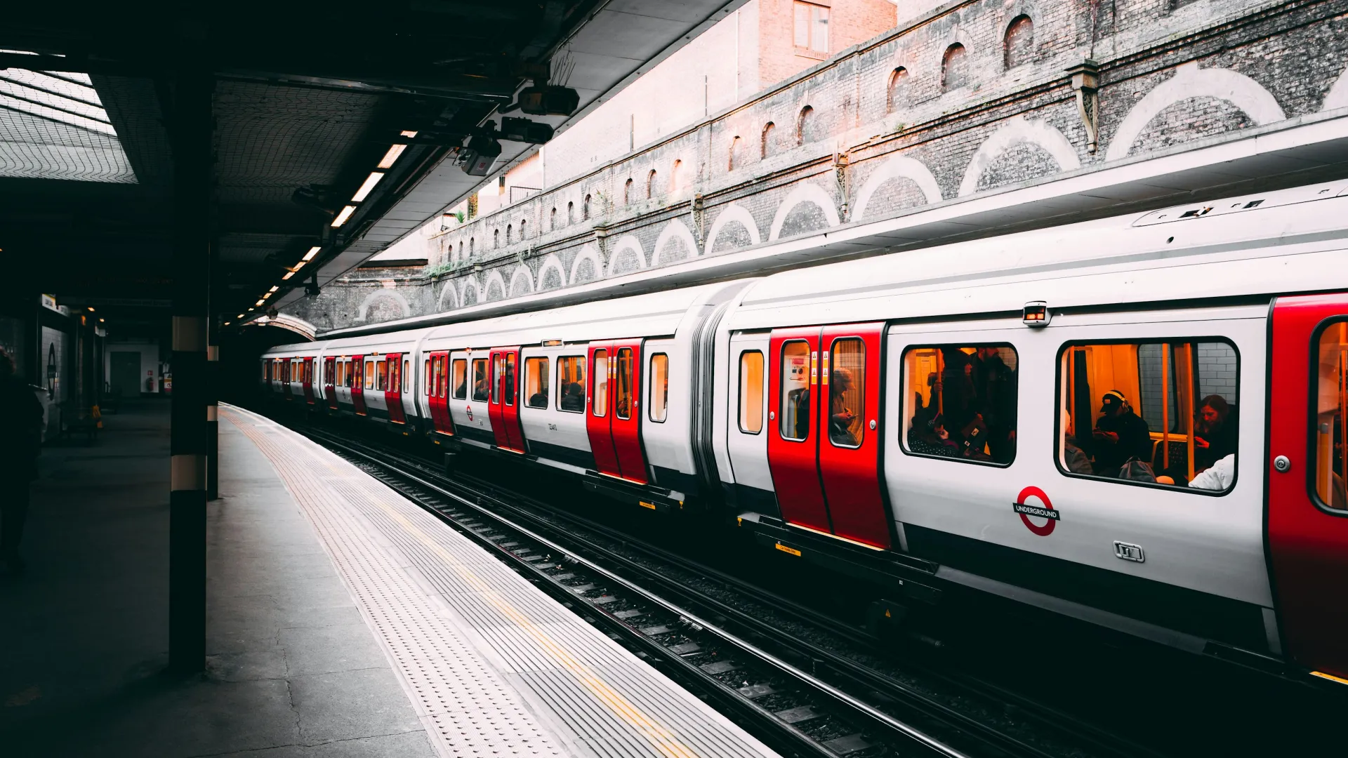 London Underground train with red doors at an empty platform in a historic brick station under natural light