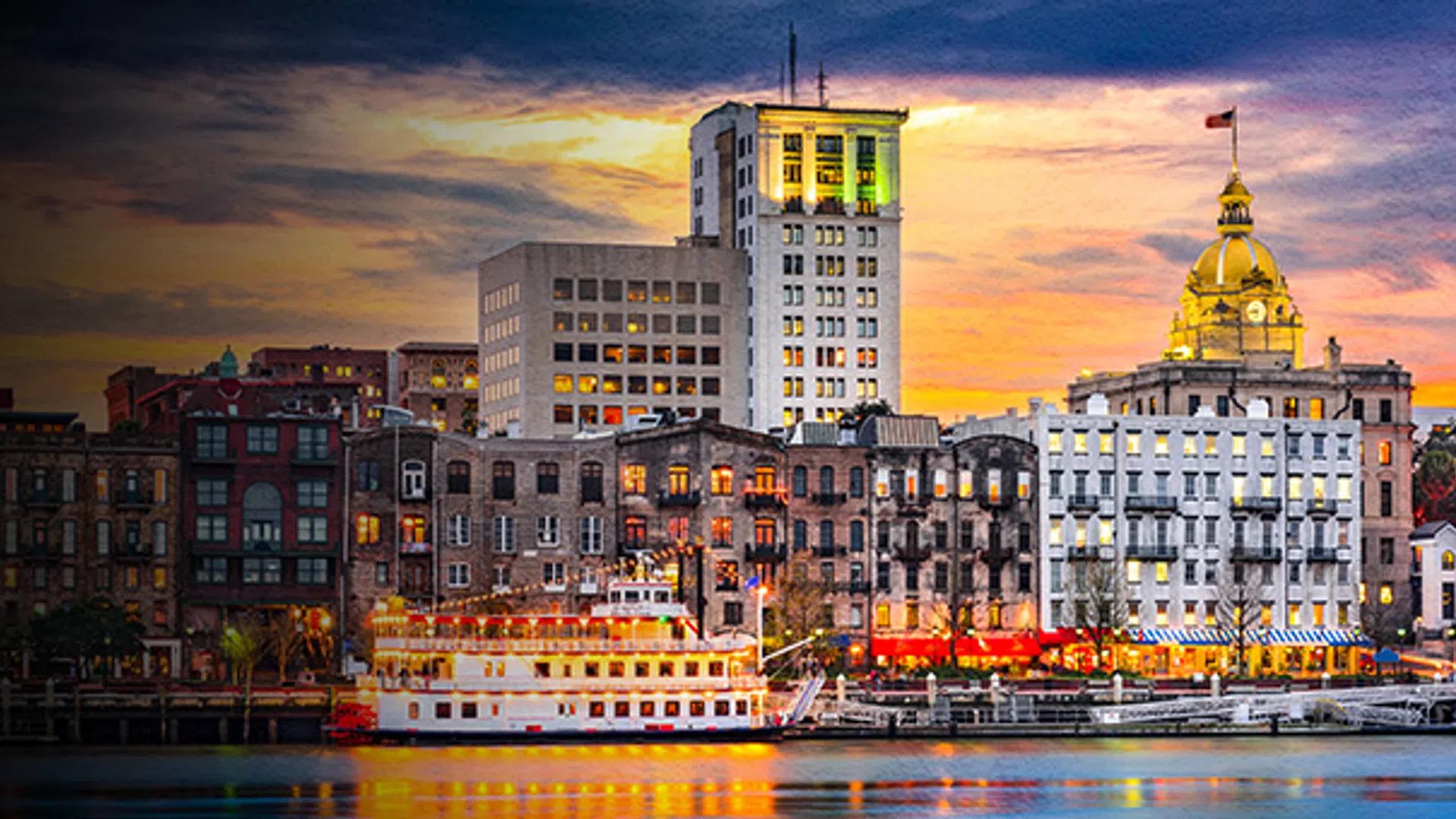 Sunset view of Savannah city skyline with illuminated historic buildings and waterfront reflections