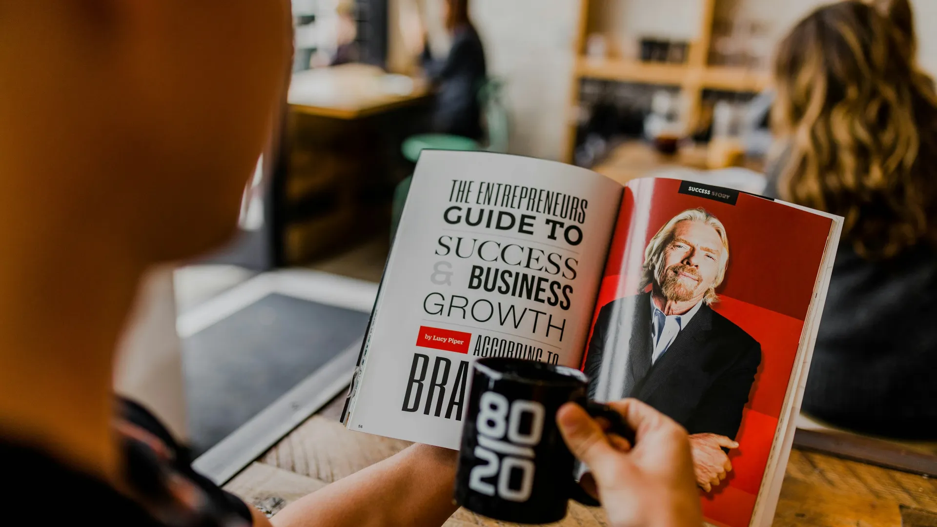 A person reading a magazine about business success while holding a coffee mug.