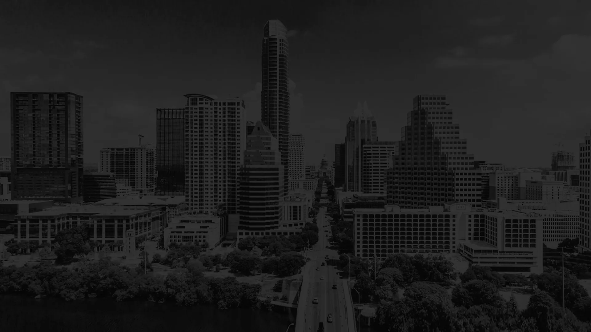 Aerial view of a city skyline with a river, bridge, and modern high-rise buildings under a cloudy sky.
