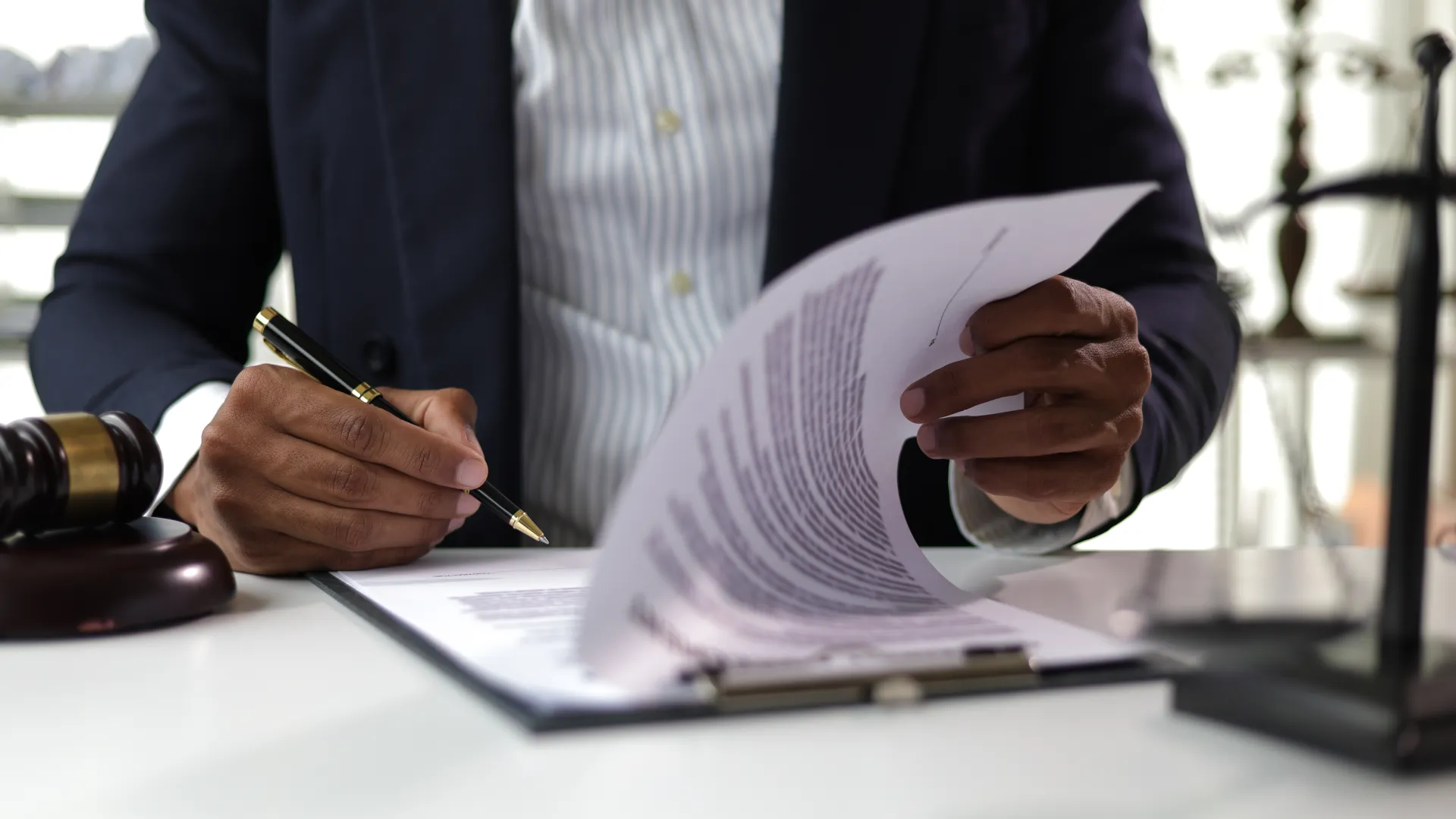 Businessman reviewing and signing legal documents at desk with gavel and scales of justice.