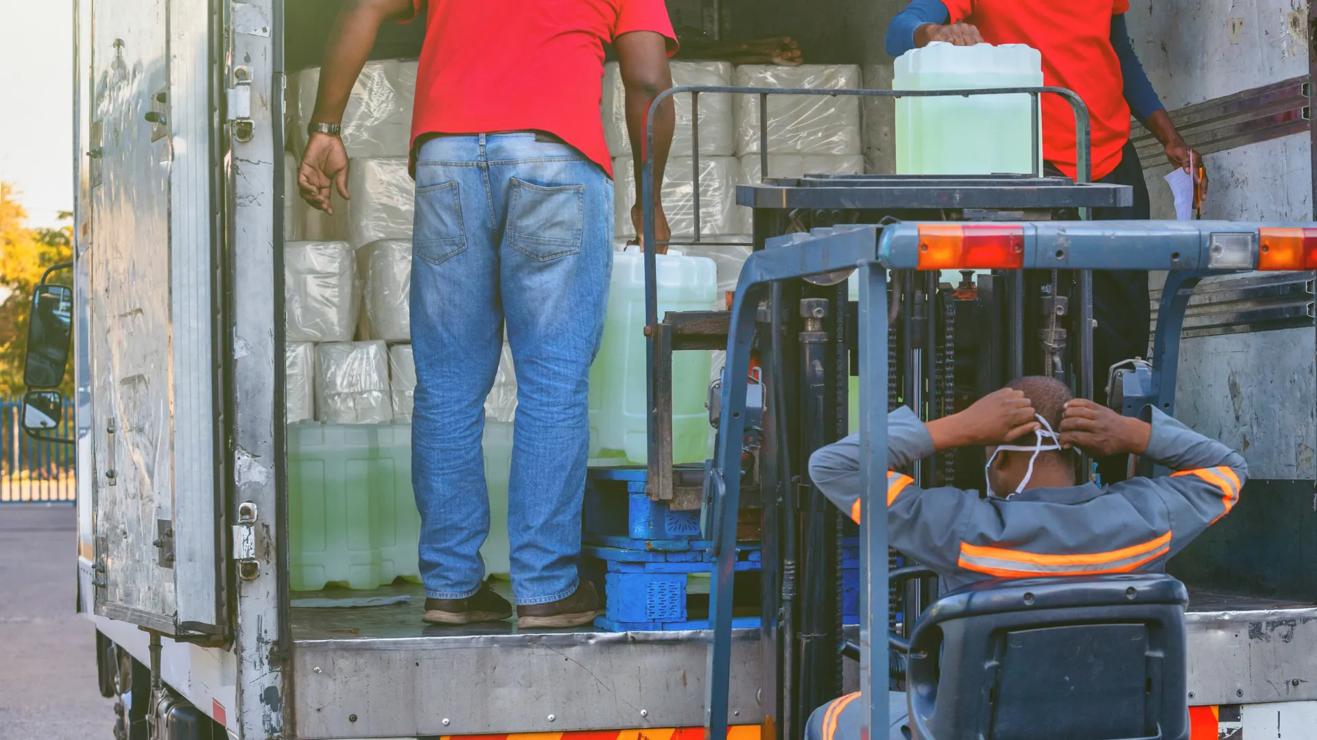 Workers loading large containers onto a truck using a forklift during a daytime delivery operation
