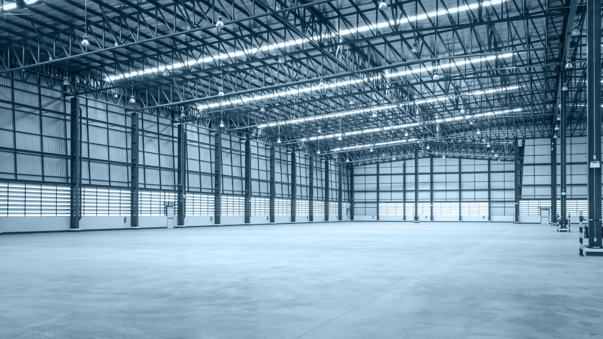 Spacious empty industrial warehouse with high ceilings, metal beams, and concrete floor under bright lighting.
