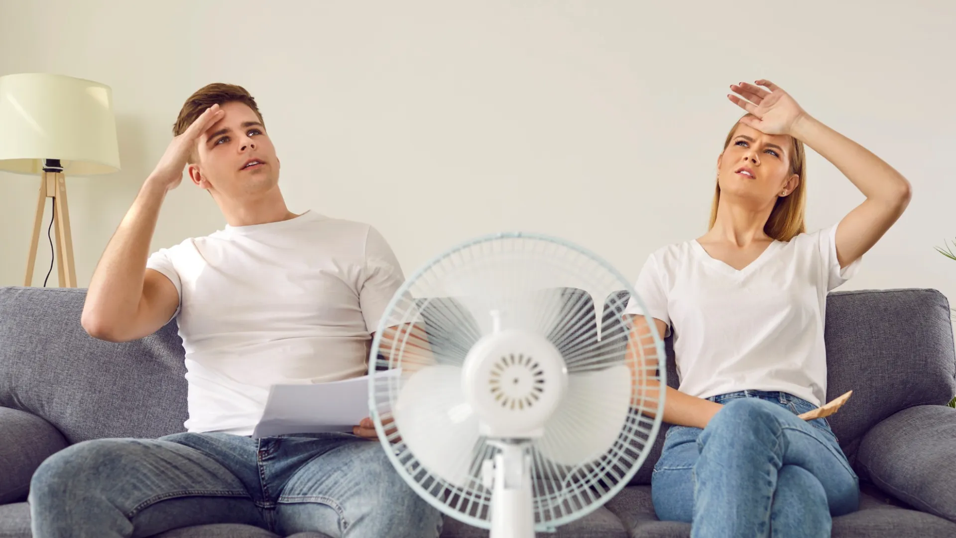 a couple of women sitting on a couch with a fan and a laptop