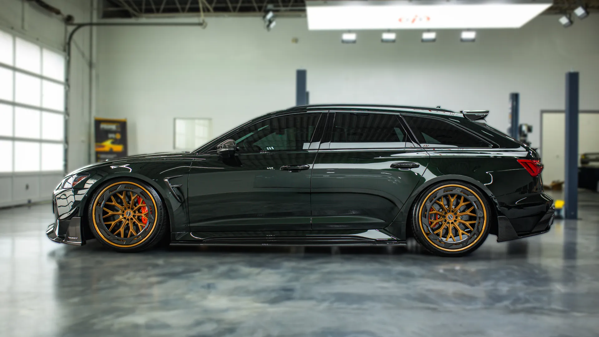 Black luxury station wagon with custom gold rims parked inside a spacious automotive garage.