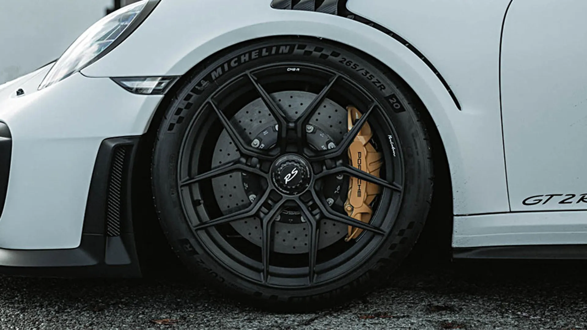 Close-up of a white Porsche GT2 RS front wheel with black alloy rim and yellow brake caliper on asphalt.