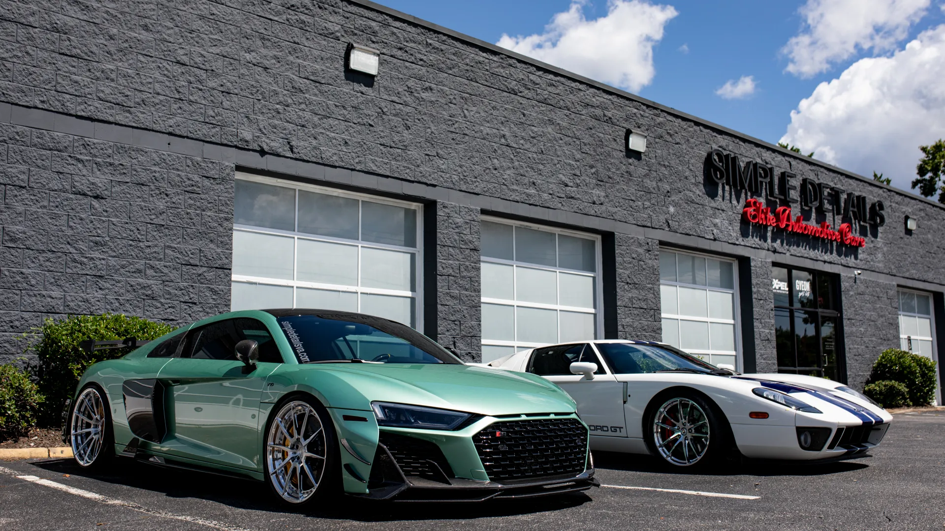 Green Audi R8 and white Ford GT sports cars parked outside Simple Details car detailing shop on a sunny day