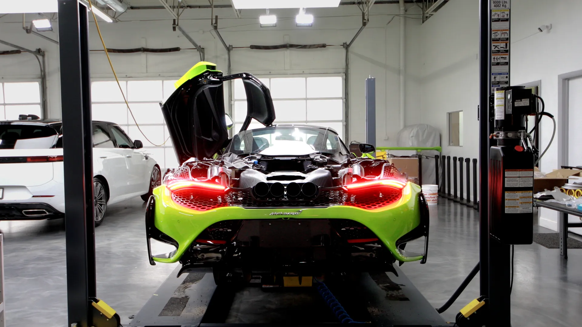 Bright green McLaren sports car with butterfly doors open inside a modern garage with another white car nearby