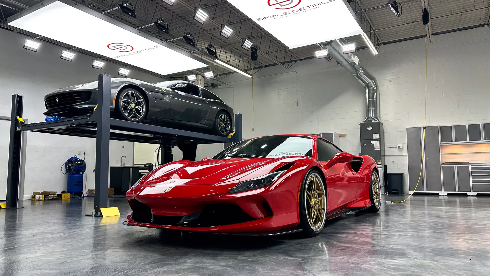 Red sports car with gold rims in a clean garage with gray car on a lift and polished concrete floor