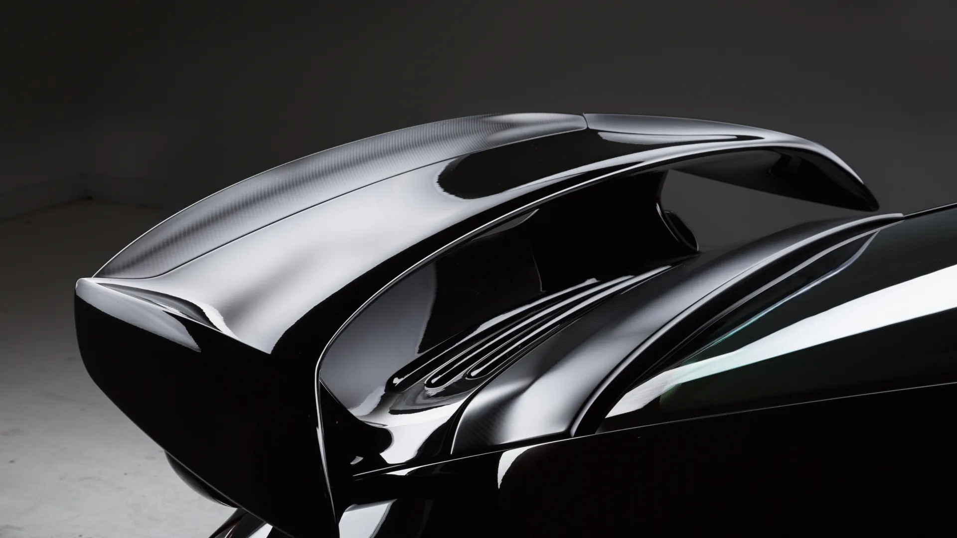 Close-up of a sleek black car rear spoiler with glossy finish and aerodynamic design against a neutral background