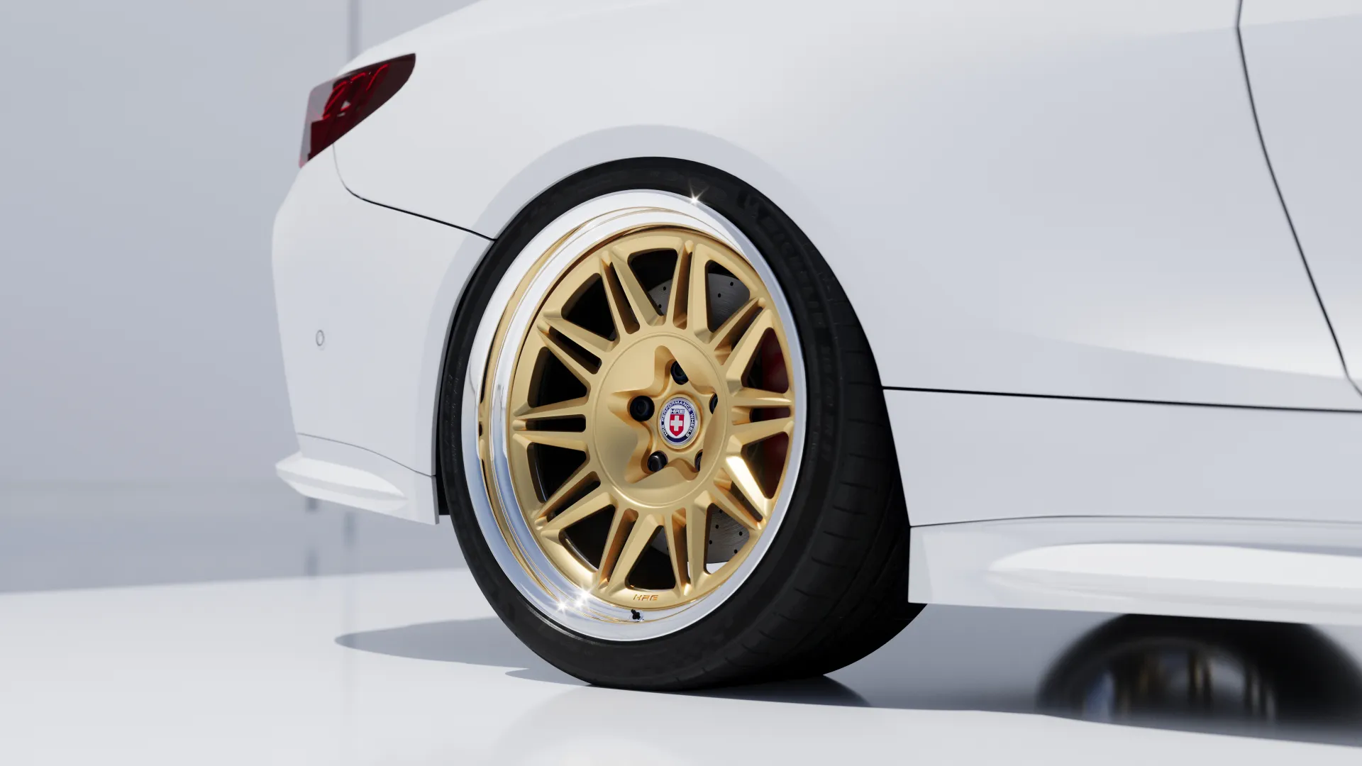 Close-up of a white car's rear with custom gold alloy wheel and low-profile tire on a clean background.