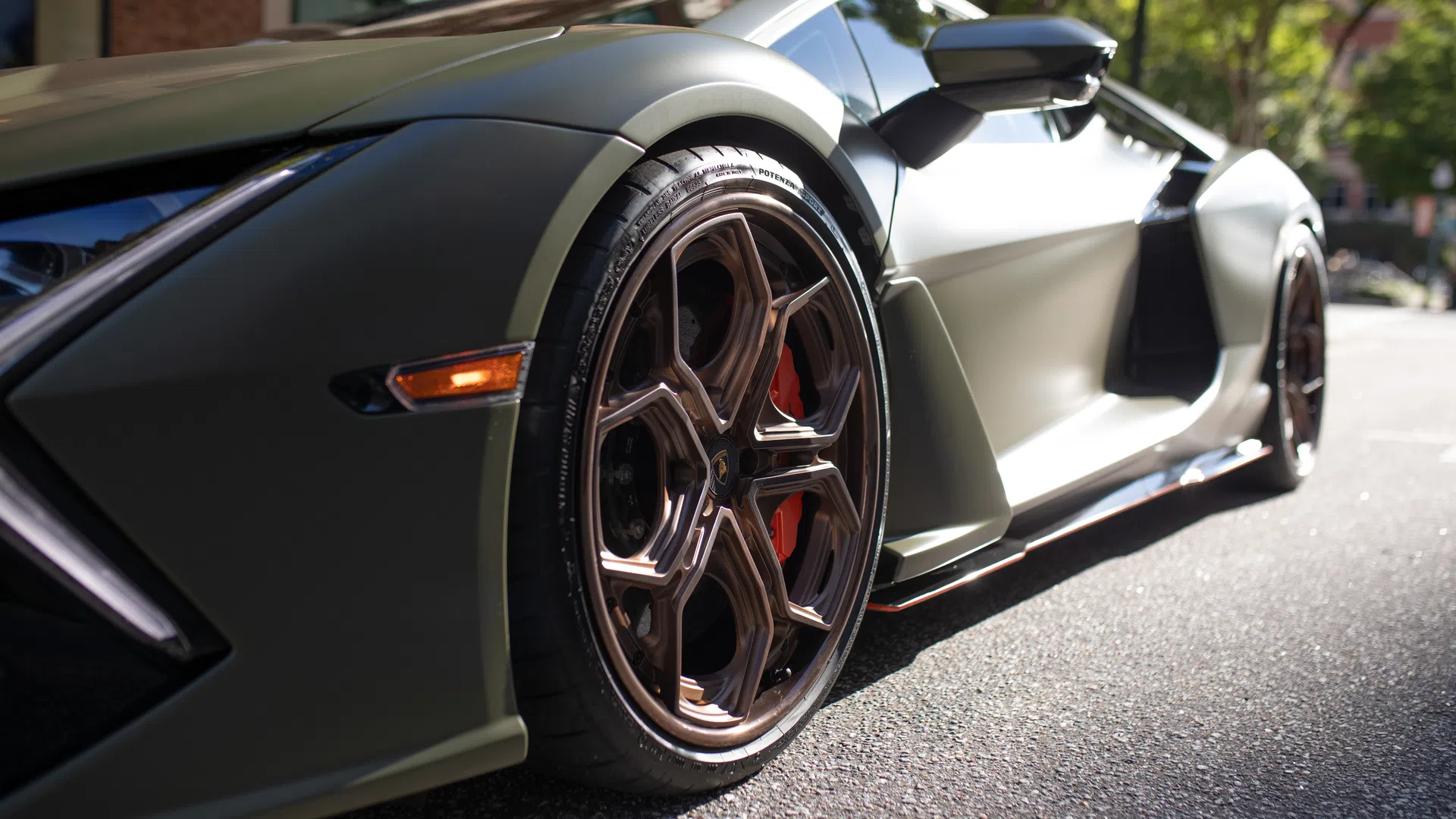 Close-up of matte green luxury sports car wheel and side, showcasing sleek design and high-performance brake calipers