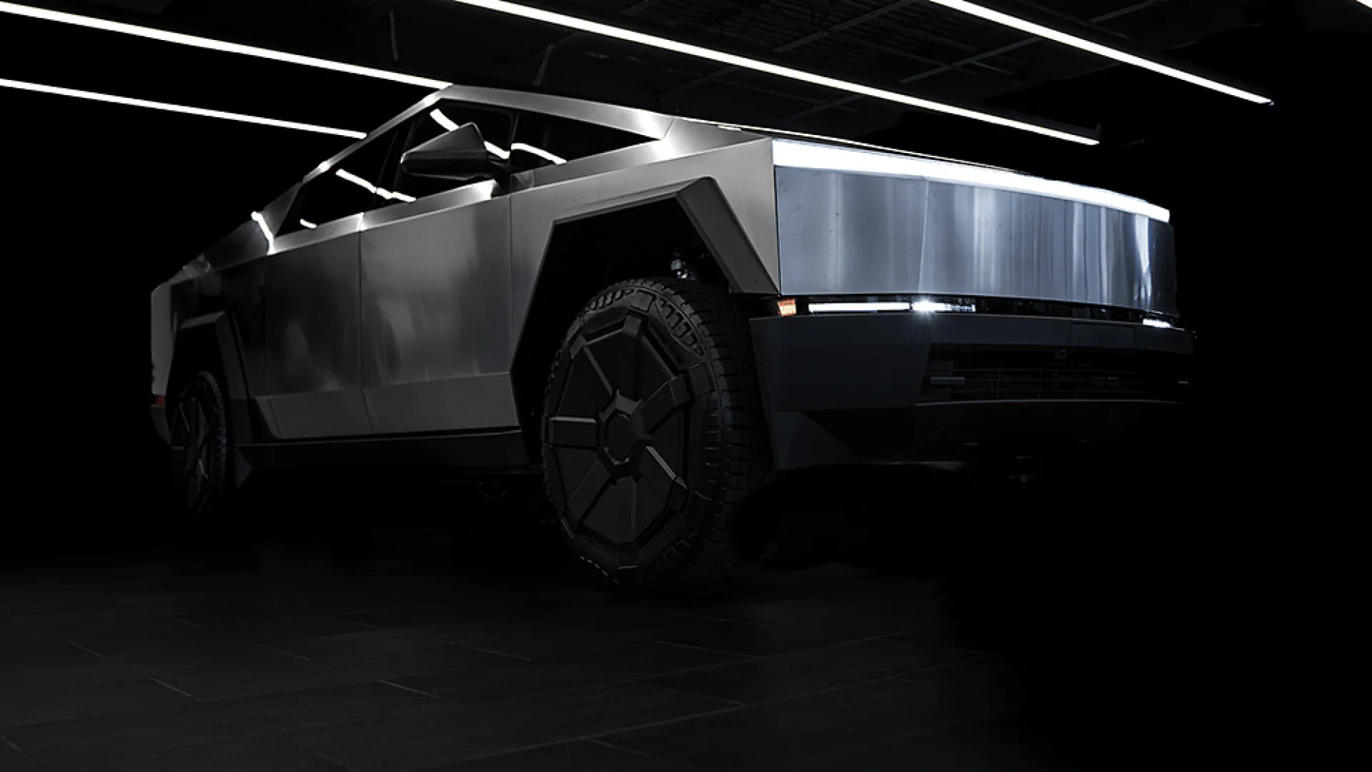 Futuristic metallic electric truck with angular design and illuminated front light bar in dark room
