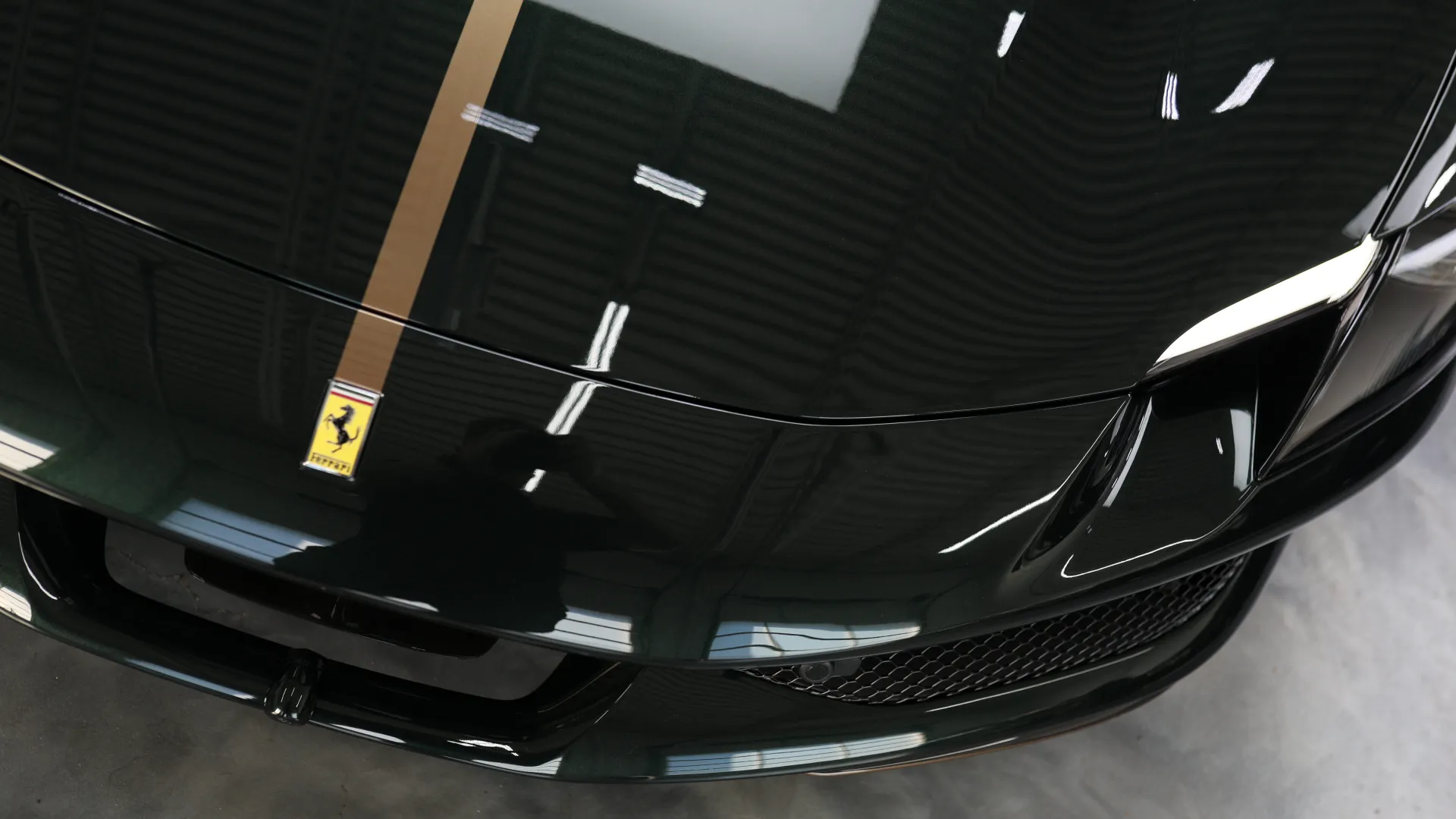 Close-up view of a glossy black Ferrari sports car hood with emblem and aerodynamic details in a showroom.