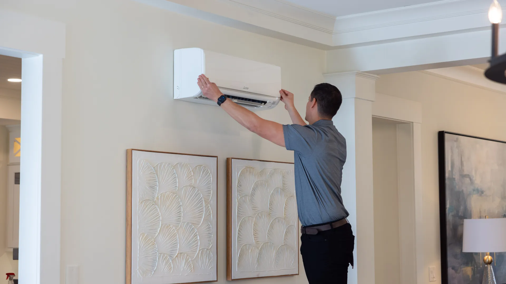 Technician installing or servicing a wall-mounted air conditioning unit in a modern living room with framed artwork