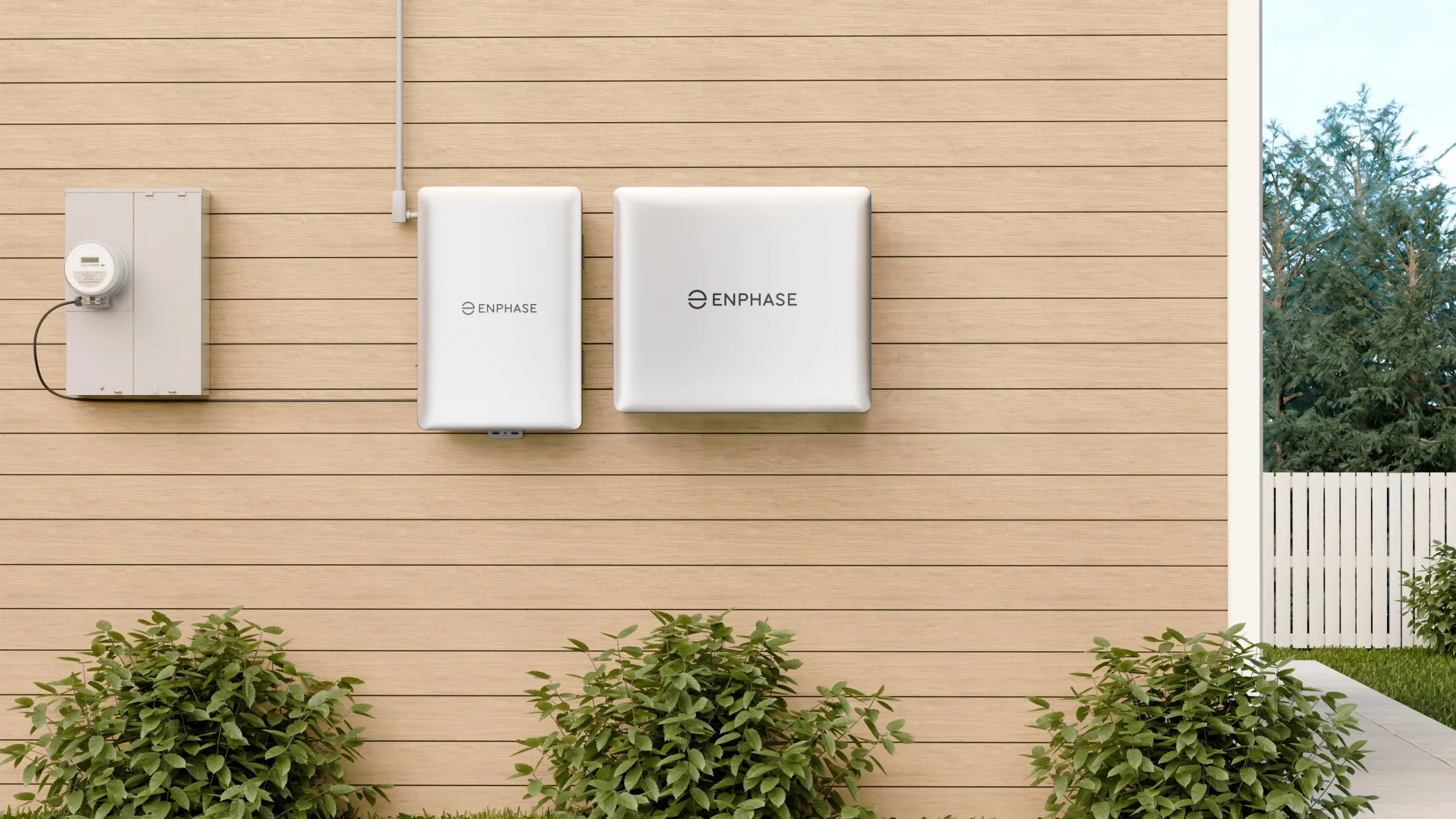Enphase solar energy system components mounted on a light wood exterior wall above green shrubs in a backyard.