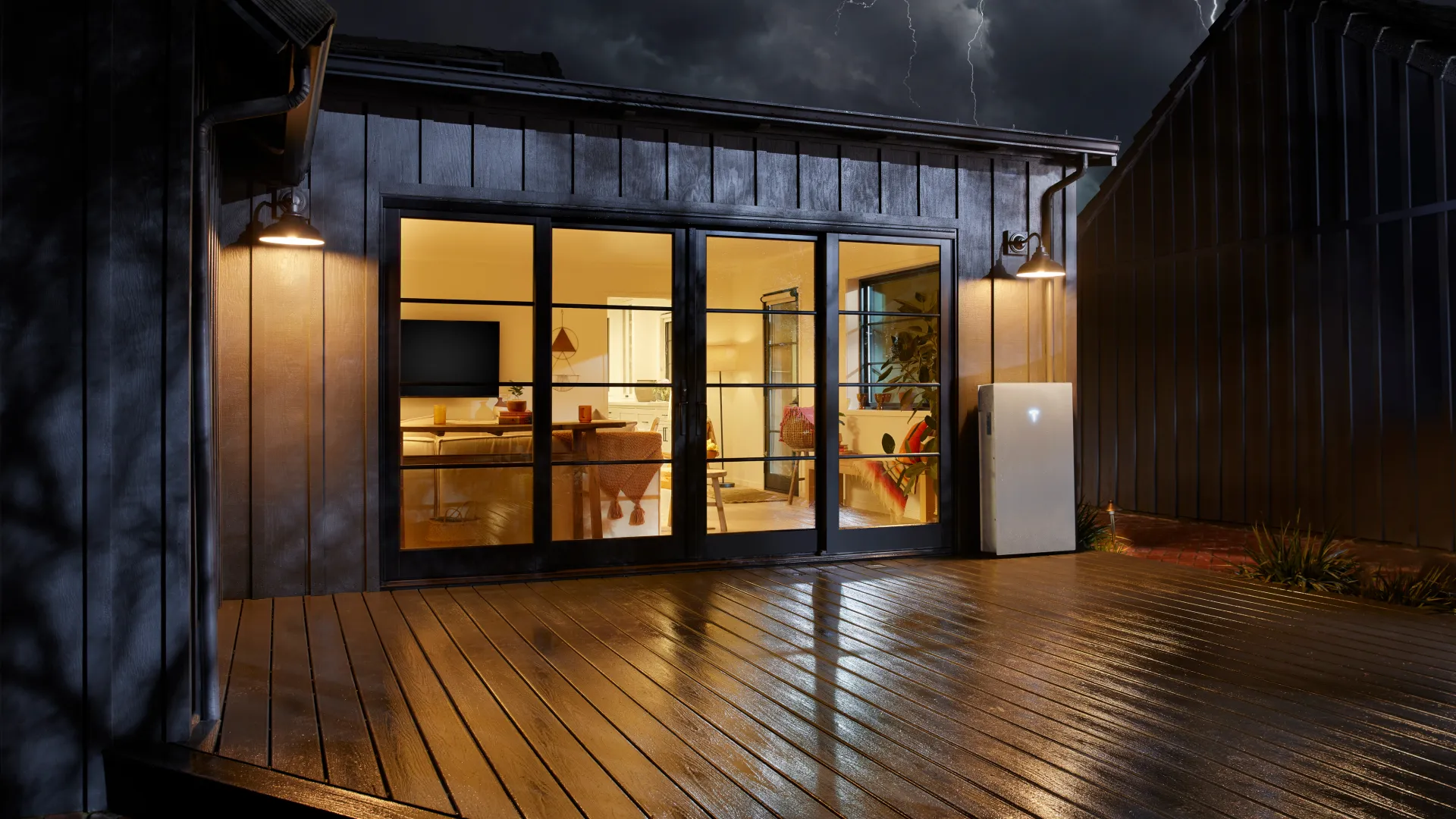Modern house patio with large glass doors lit warmly as lightning strikes in stormy night sky above.