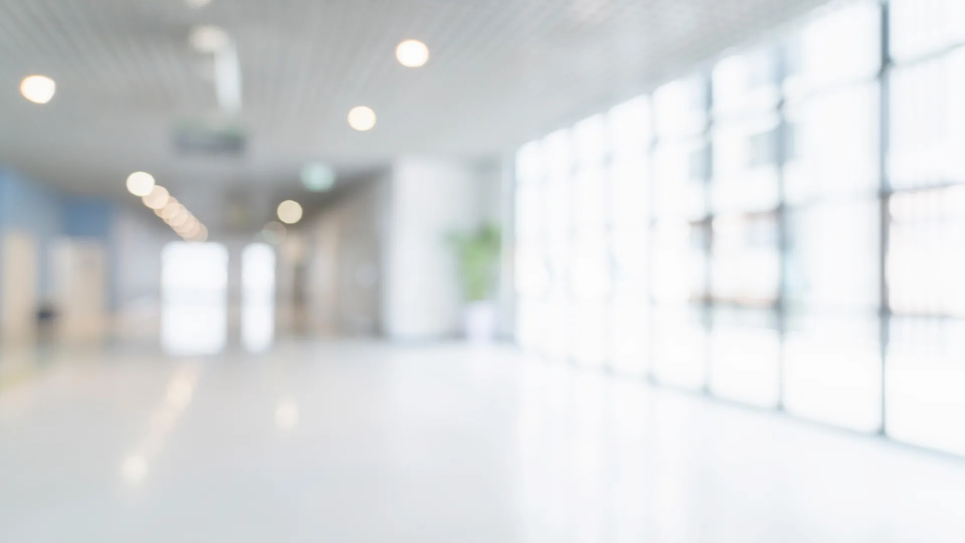 Bright, spacious corridor with large windows and overhead lights in a modern building interior.