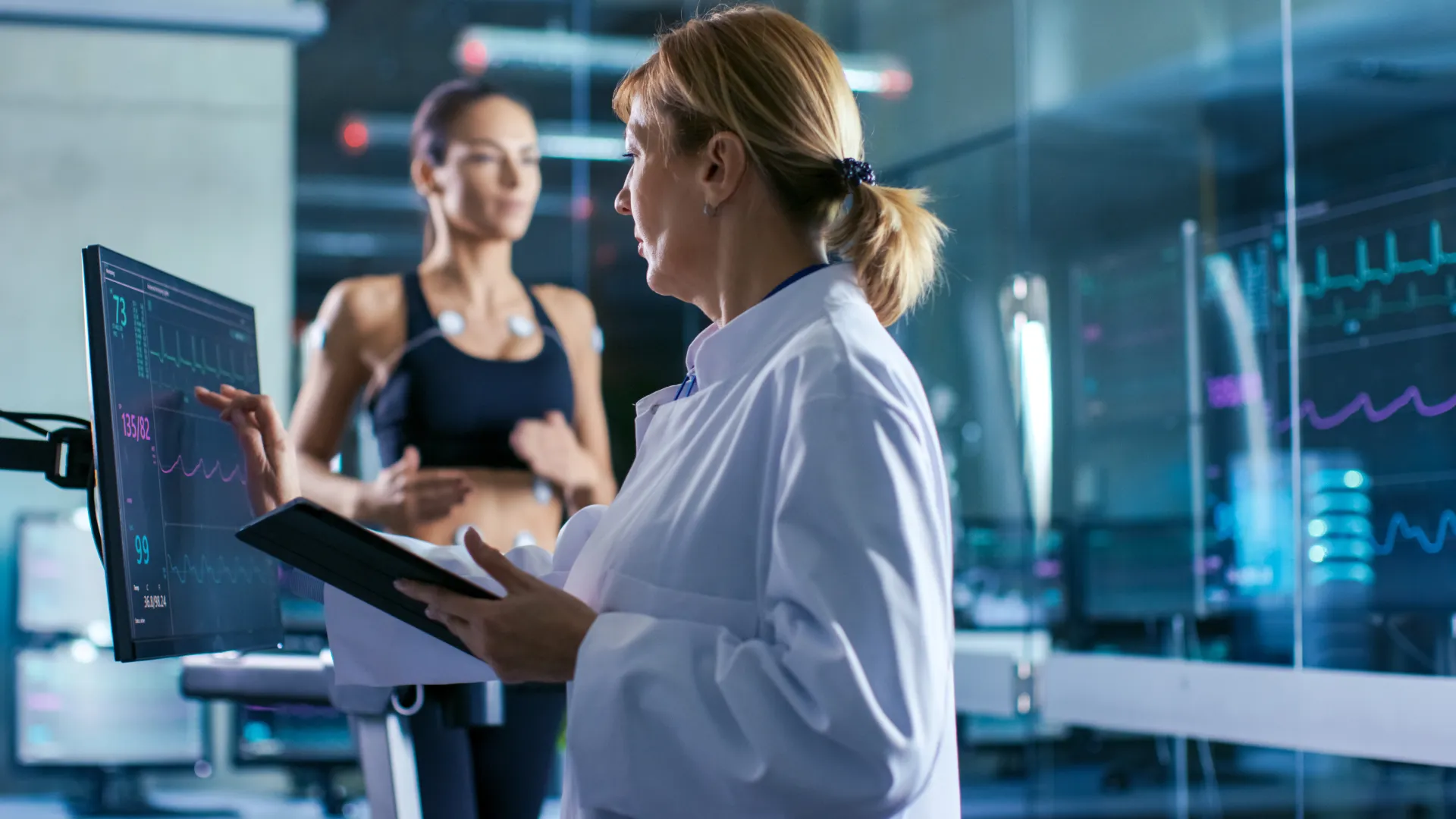 Doctor monitoring female athlete's heart rate and vitals on screen during fitness test in medical lab.