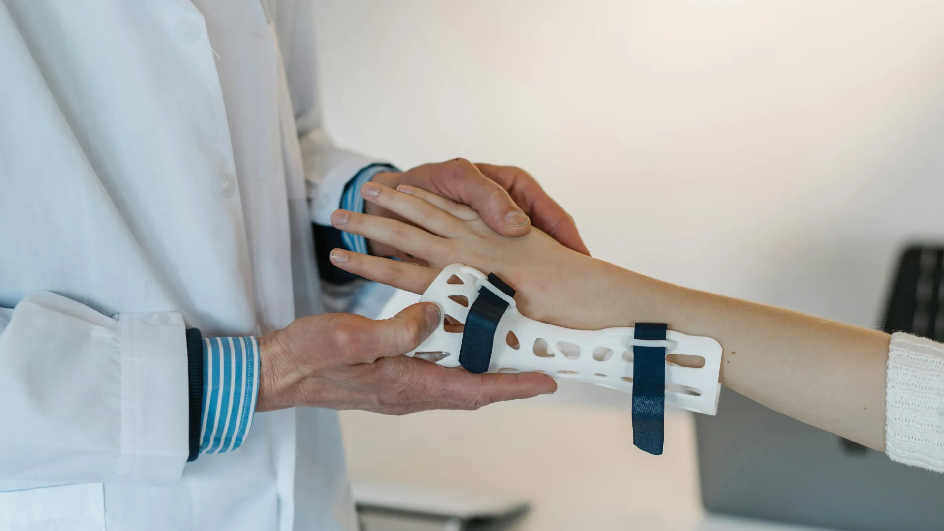 Doctor fitting a white wrist brace with blue straps on patient’s arm in a clinical setting.