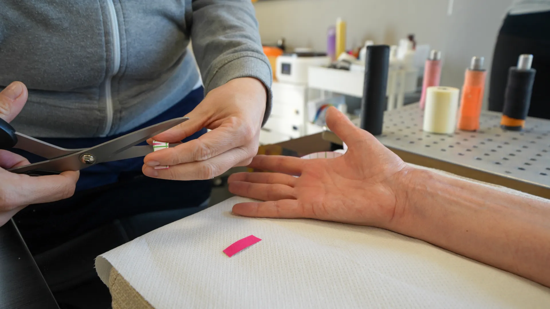 Person cutting a small piece of paper or tape with scissors near an outstretched hand on a table.
