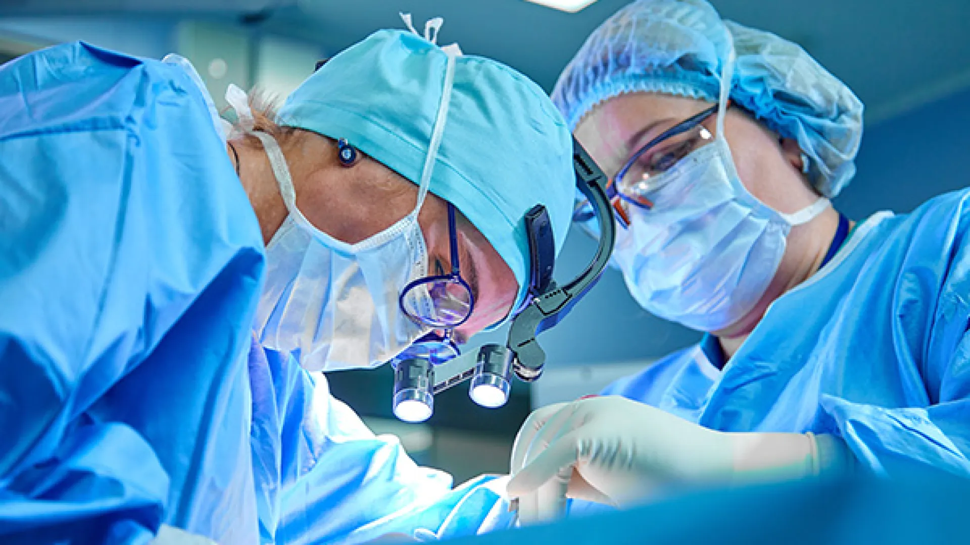Two surgeons wearing surgical masks and blue scrubs performing an operation in a sterile operating room.