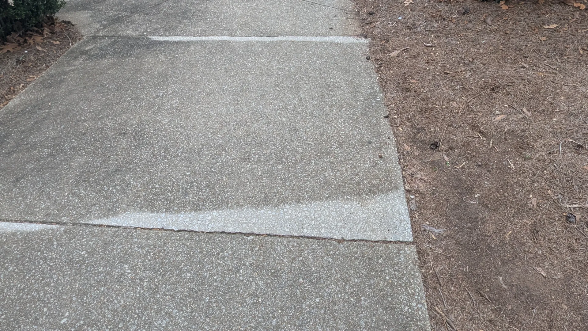 Sidewalk leading past parked cars and bushes on a cloudy day with one shoe visible at the bottom edge.