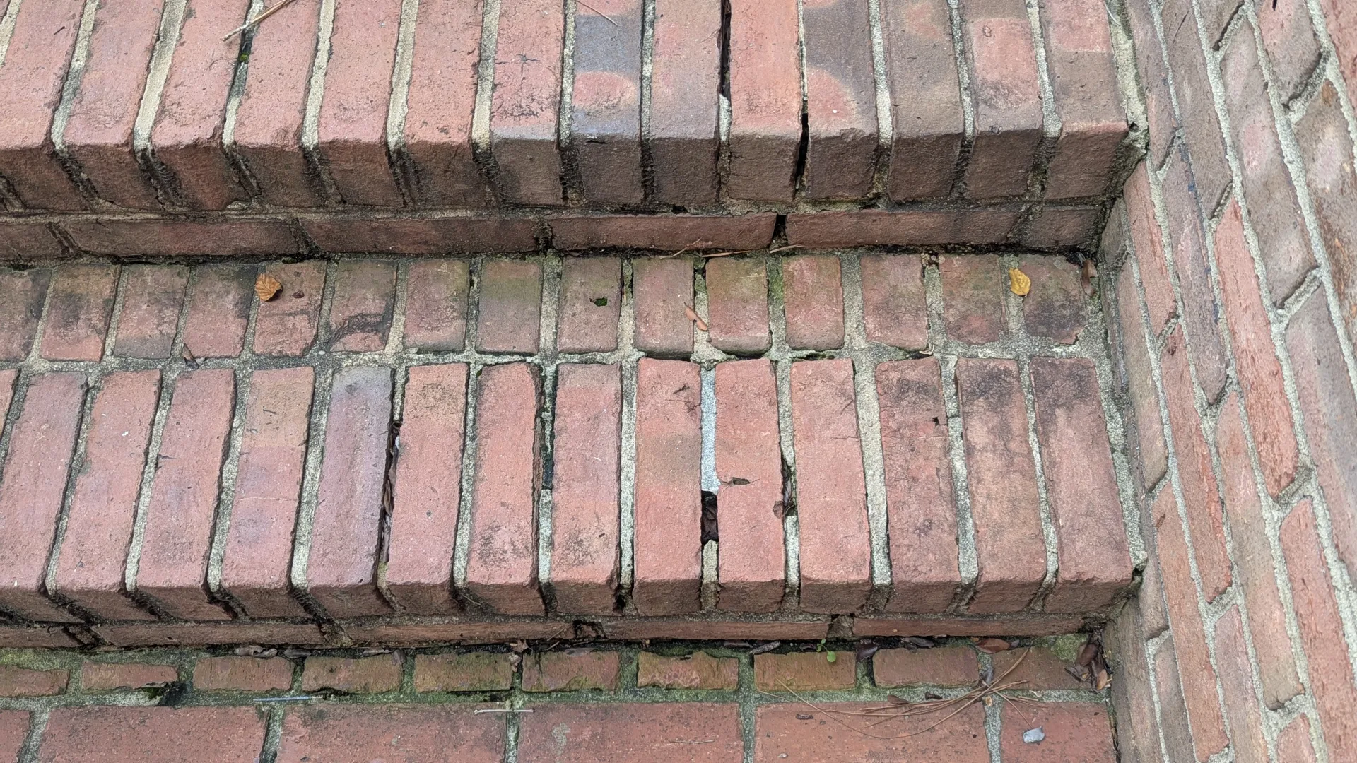 Worn red brick stairs with visible cracks and aging against a brick wall corner in outdoor setting
