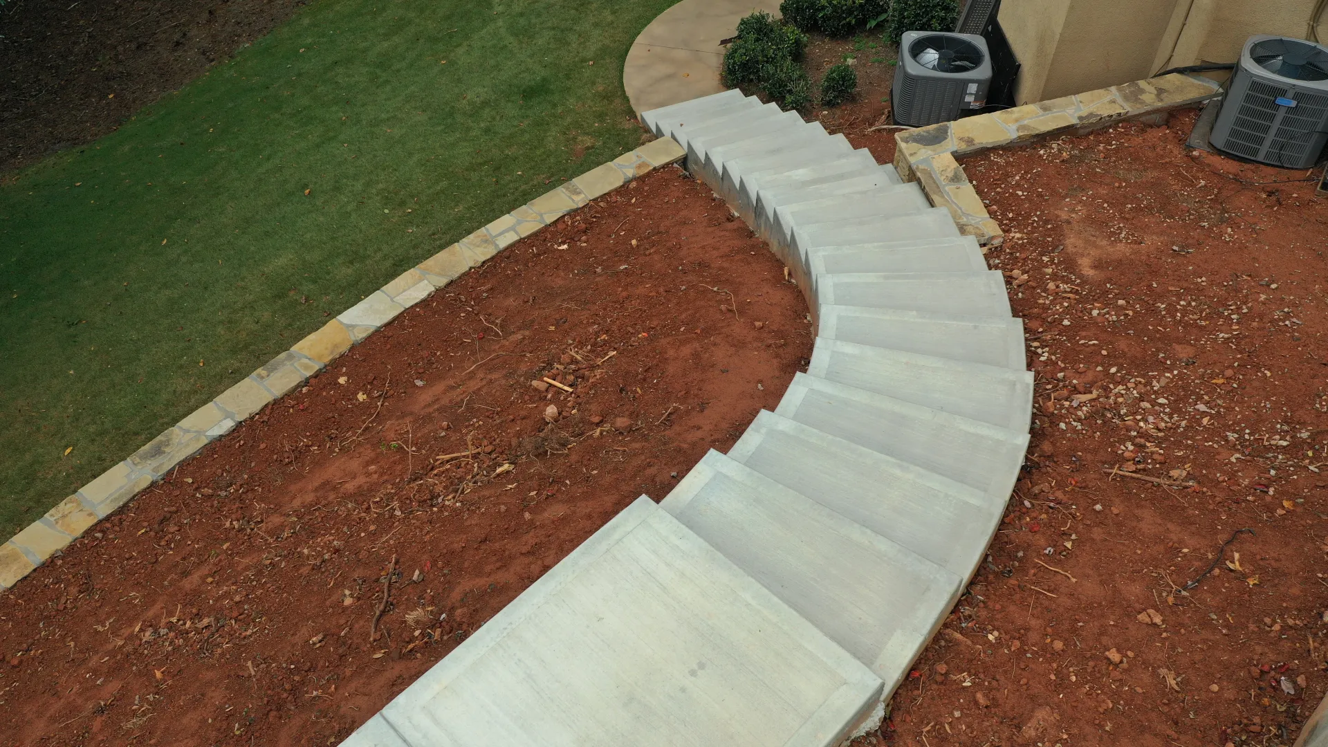 Aerial view of a modern spiral staircase leading to a landscaped area with green grass.