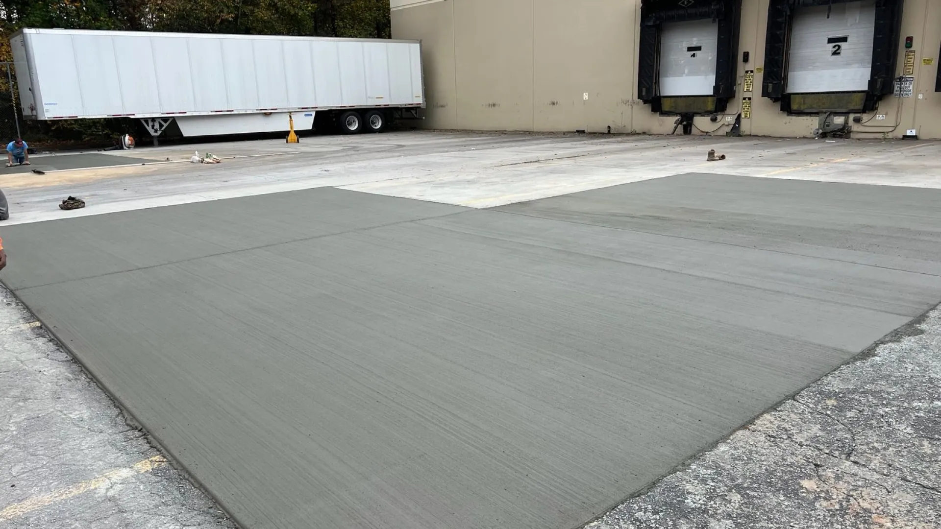 Freshly laid concrete surface in a loading dock area with delivery trucks in the background.